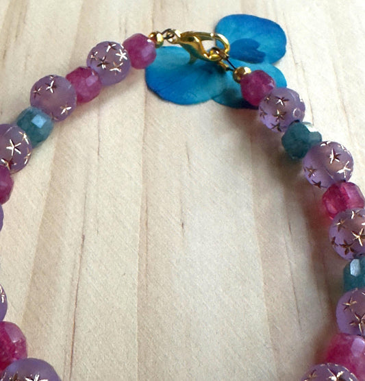 Close-up view of a lavender and teal gemstone bracelet featuring delicate gold star details on select beads.