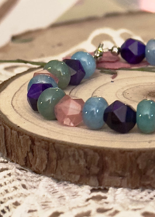 Close-up of faceted gemstone beads on a handmade bracelet resting on a natural wood slice, showing texture and color detail