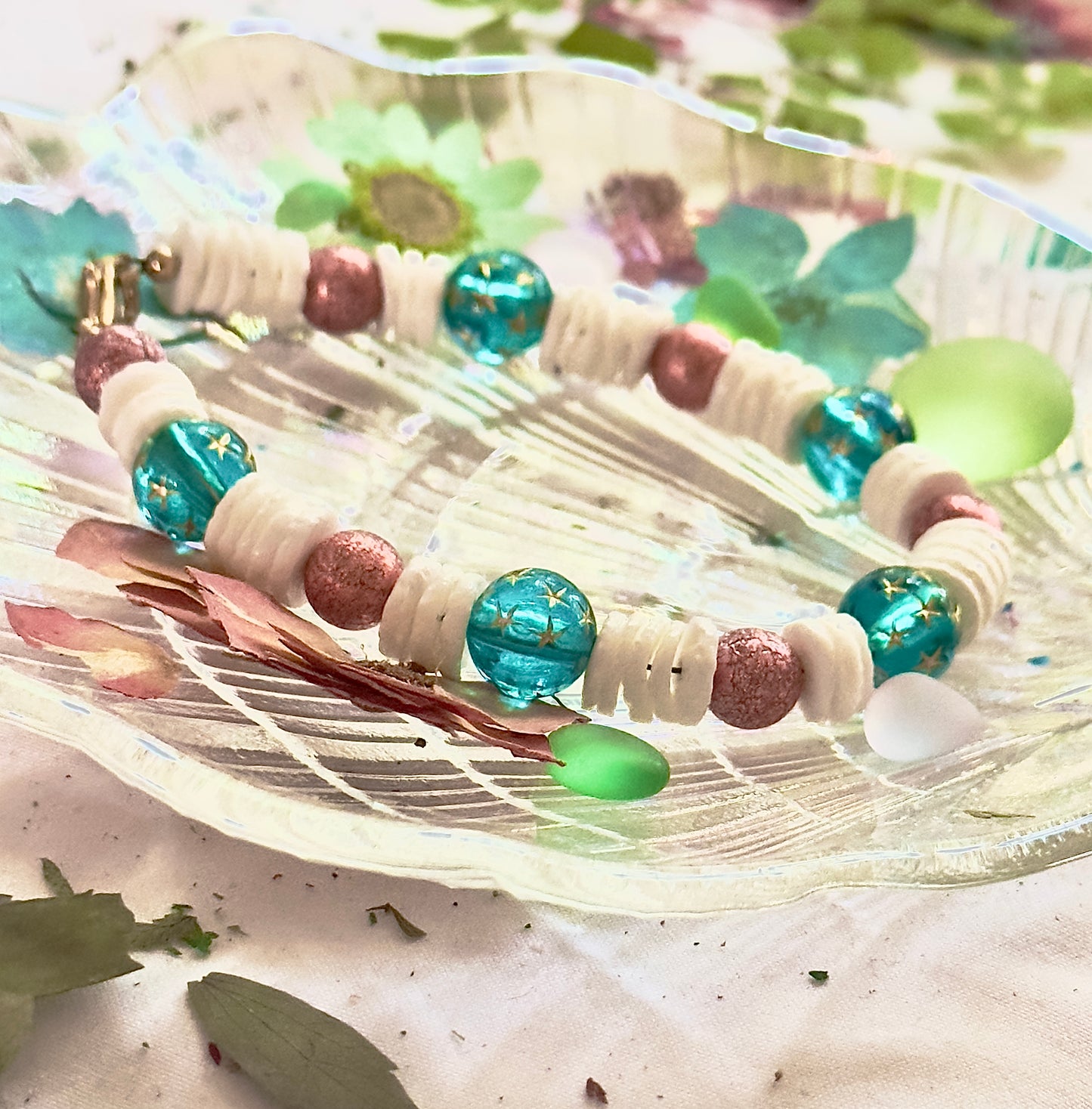 Handmade ocean-themed bracelet with teal star beads and white shell spacers styled outdoors with greenery and natural light.