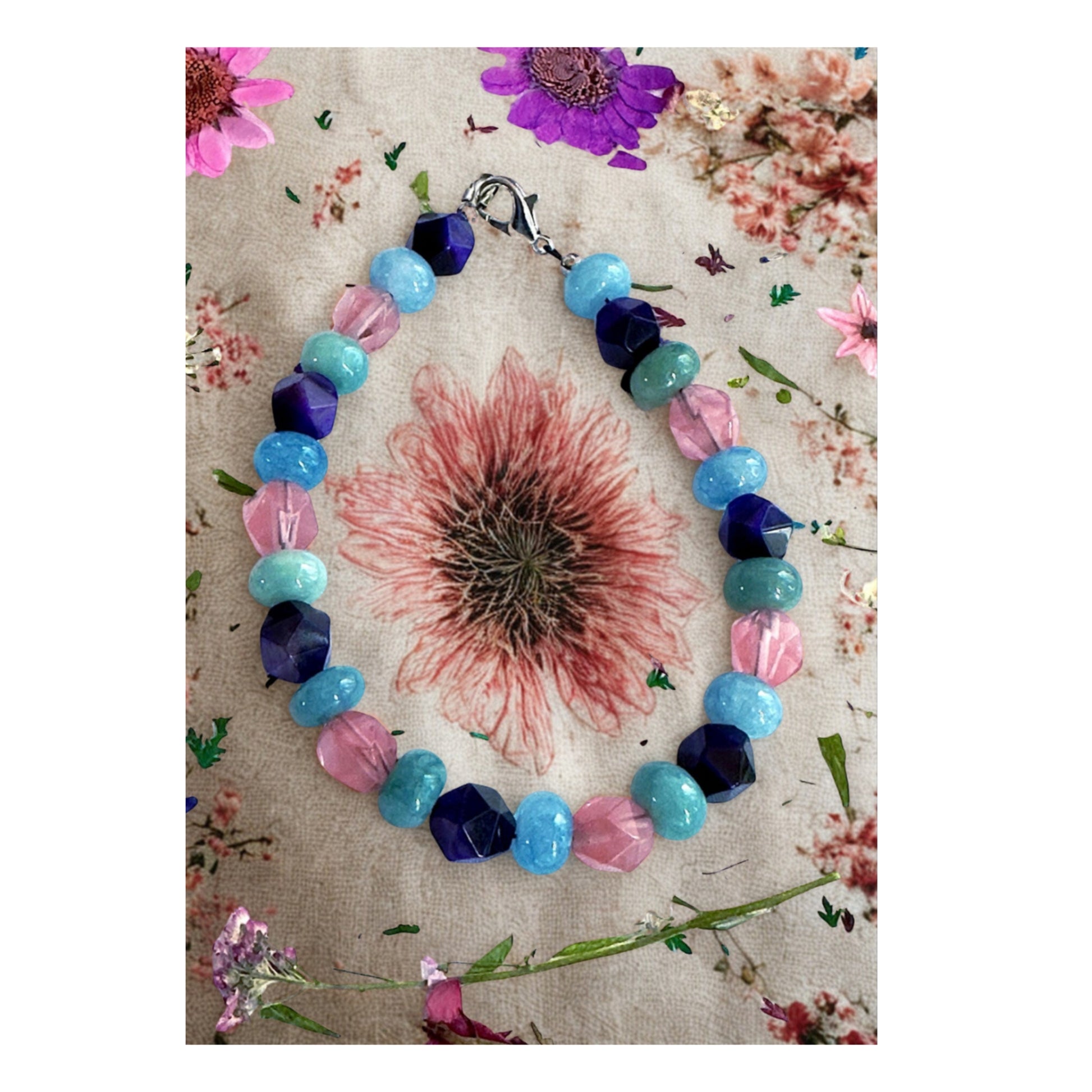 Gemstone bracelet styled on a floral background with soft pink and blue tones, feminine and calming jewelry flat lay