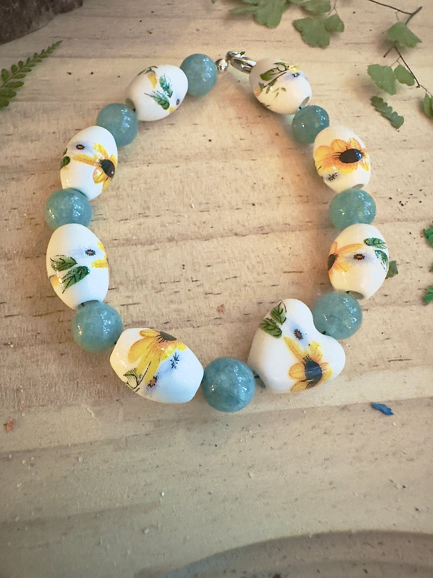 Sunflower gemstone bracelet arranged in a circle on natural wood, yellow flower beads and teal stones