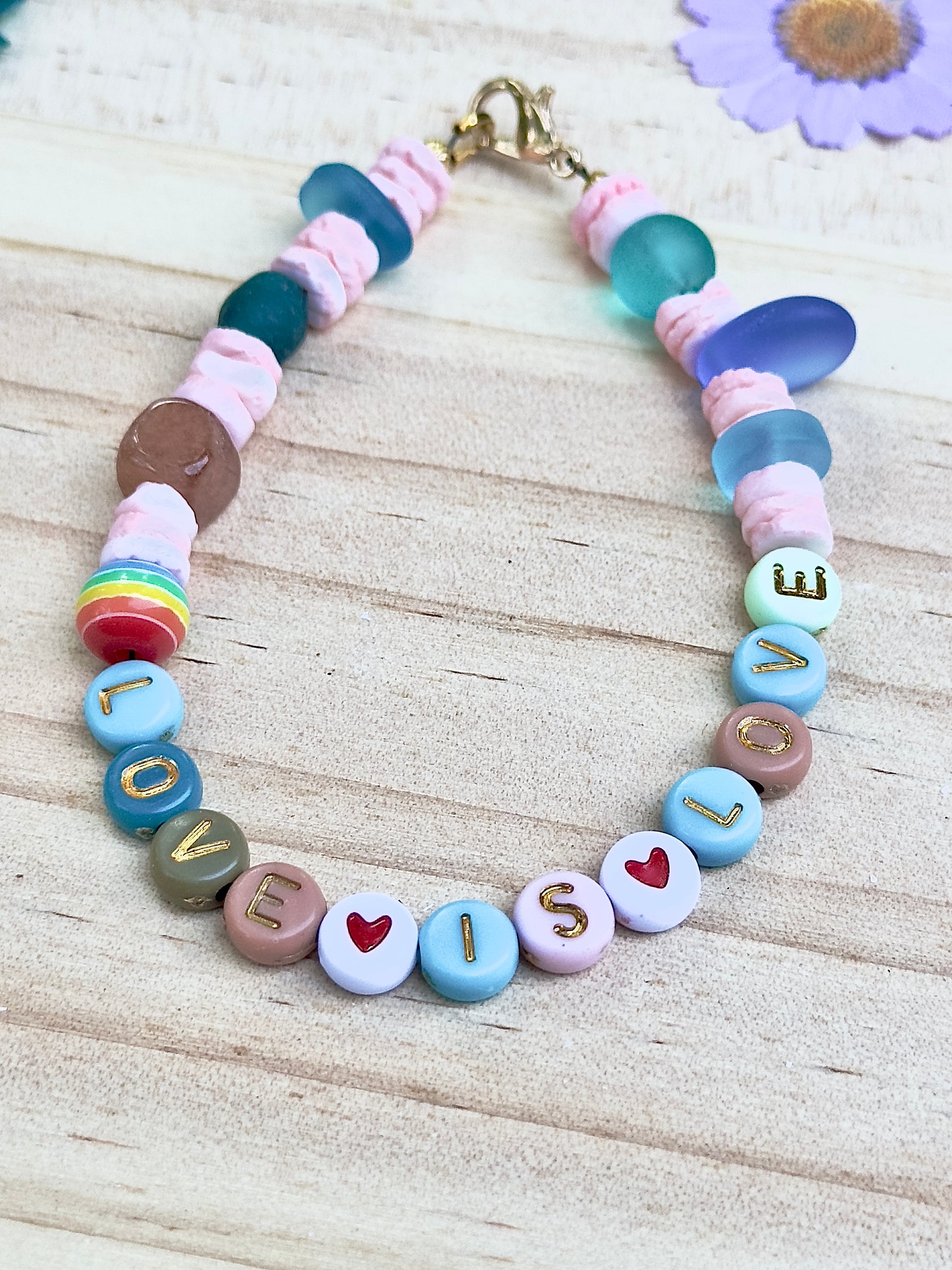 Handmade pastel beaded bracelet styled for everyday wear, featuring inclusive “LOVE IS LOVE” message and heart accents.