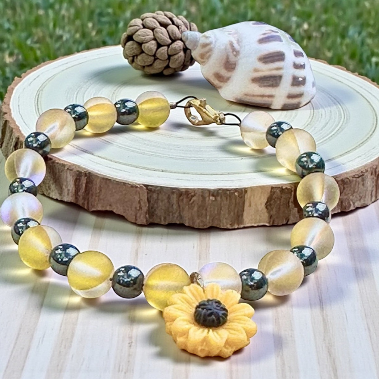 Sunflower bracelet arranged on a natural wood slice with a seashell accent, showcasing handmade craftsmanship and earthy, grounded styling.
