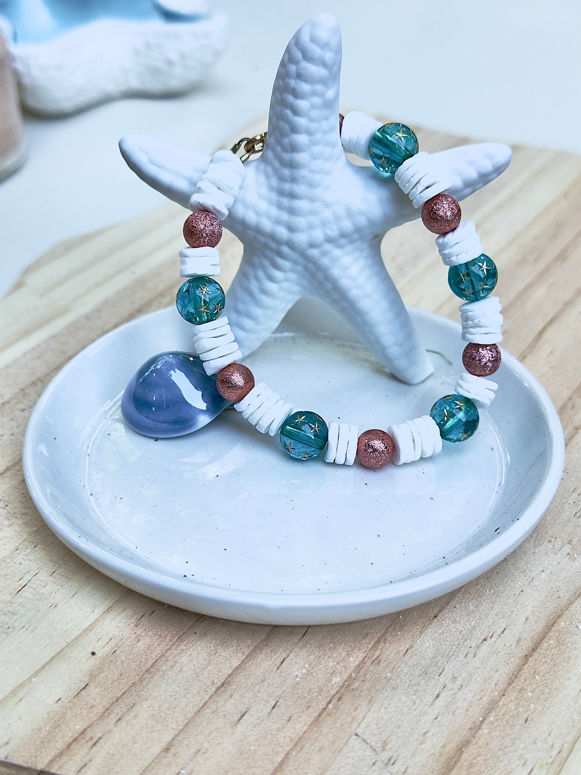 Ocean-inspired bracelet featuring teal star-pattern beads and rose shimmer accents shown from a different angle on a starfish-shaped dish.
