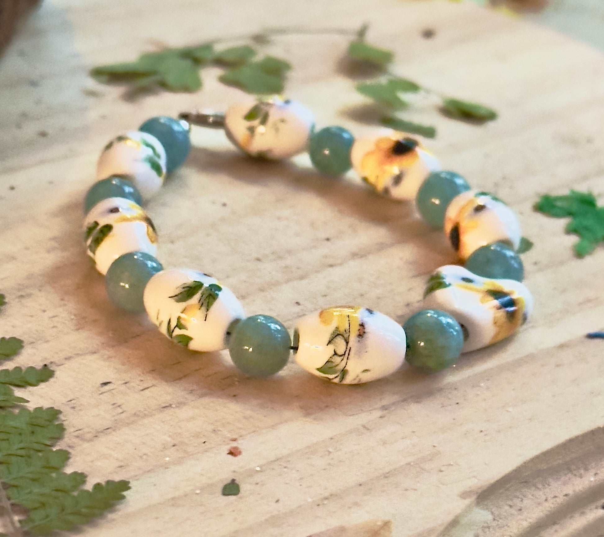 Handmade sunflower beaded bracelet on wooden surface, yellow floral beads with teal gemstone accents