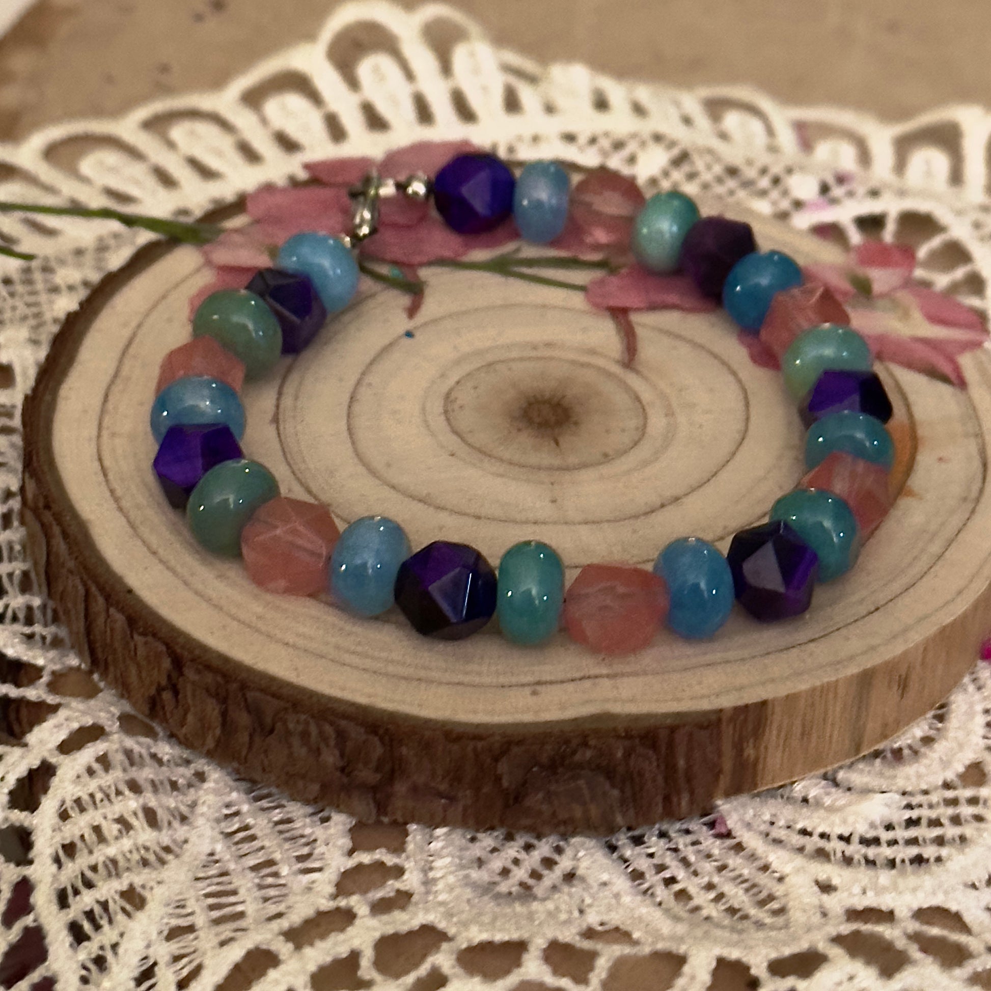 Beaded gemstone bracelet resting on lace and wood surface, cozy handmade jewelry aesthetic