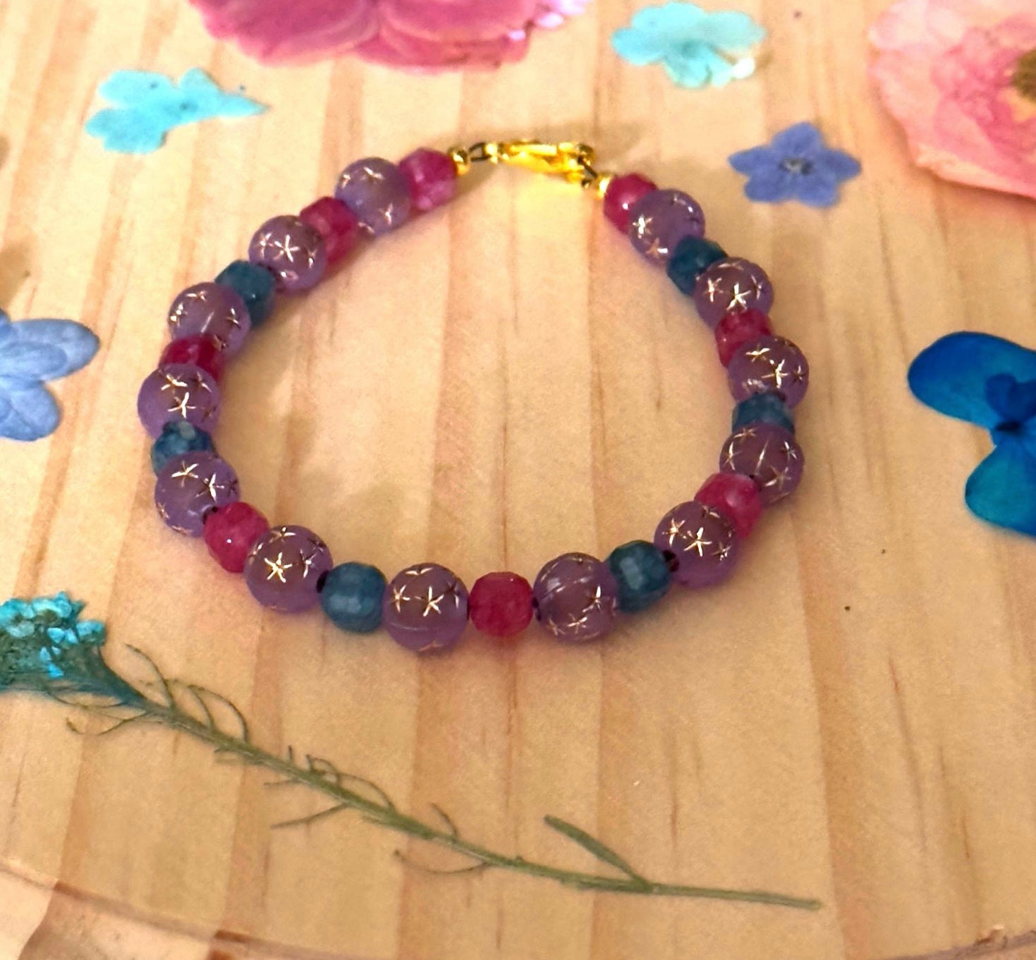 Lavender and teal star bead bracelet styled on a warm wood surface with a soft, natural aesthetic.