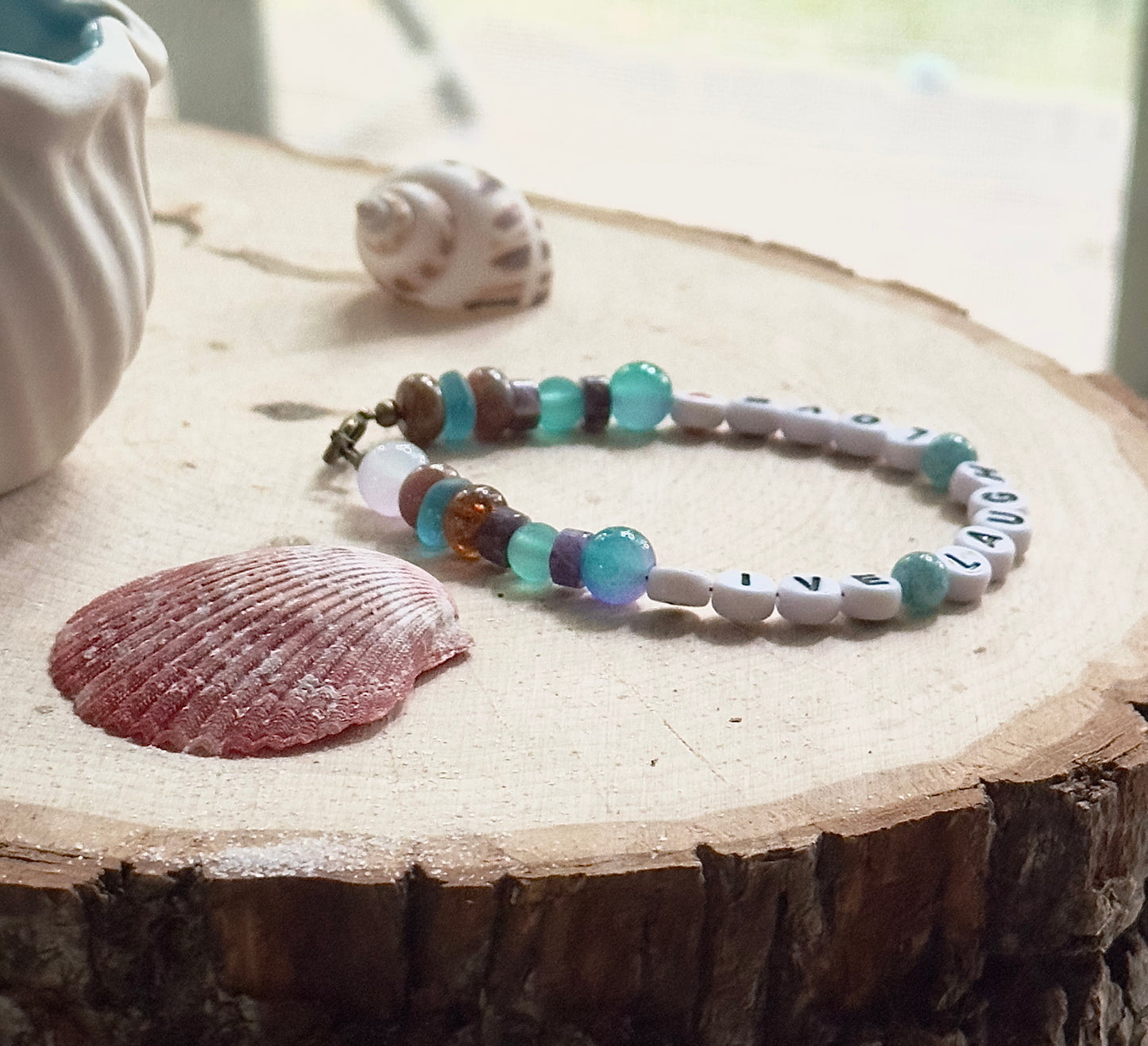 Angled view of a handmade Live Laugh Love bracelet highlighting the curved shape and balanced gemstone accents.
