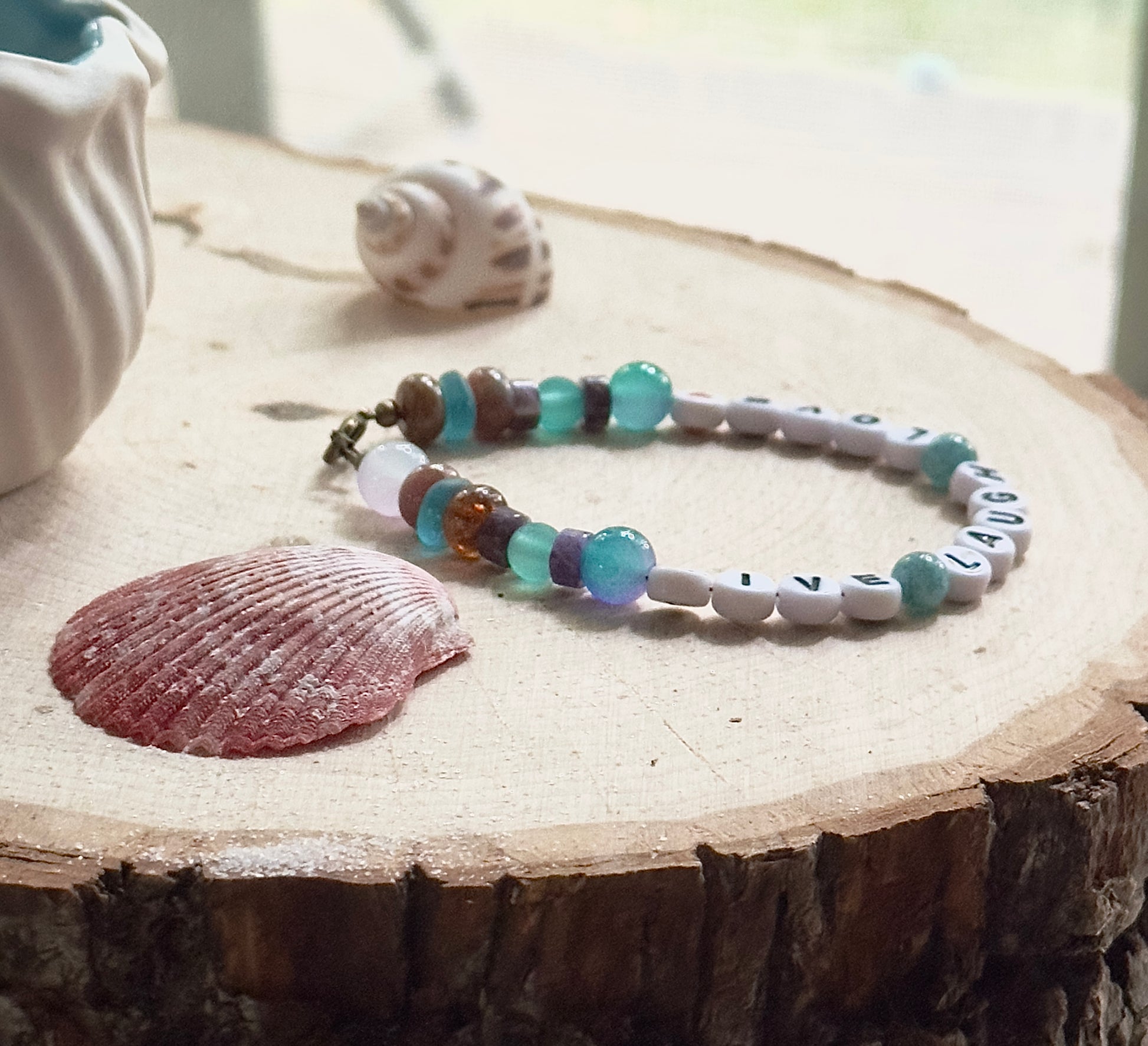 Angled view of a handmade Live Laugh Love bracelet highlighting the curved shape and balanced gemstone accents.
