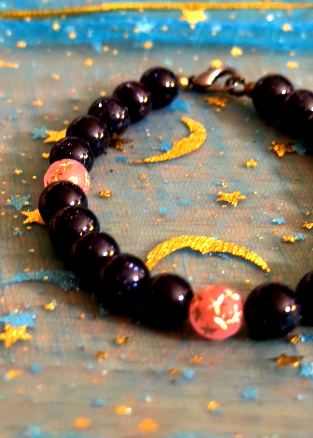 Celestial gemstone bracelet arranged on a starry moon-themed background, featuring deep blue sandstone and soft pink accent beads
