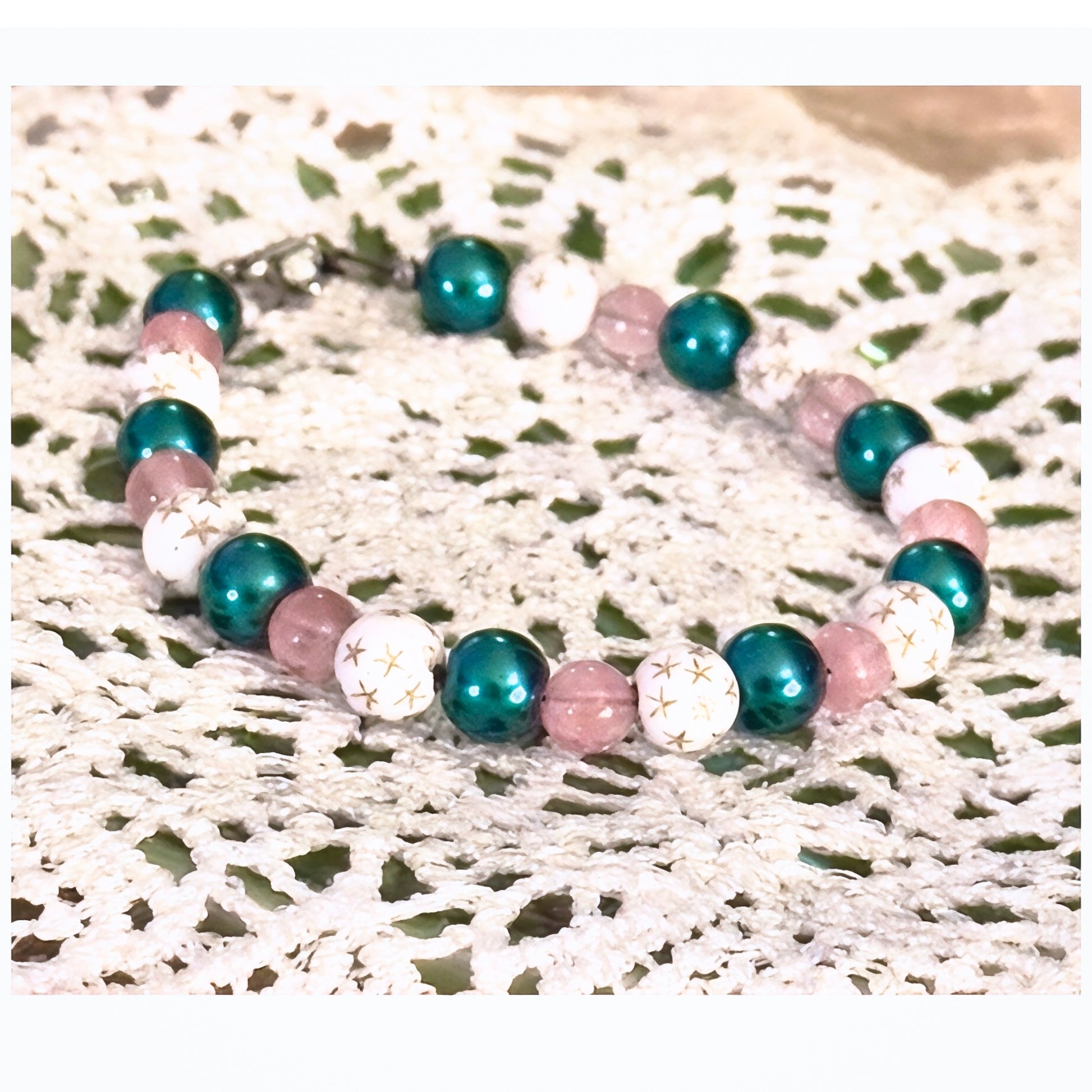 Close-up of a handmade beaded bracelet featuring teal pearls, pink beads, and white beads with star designs

