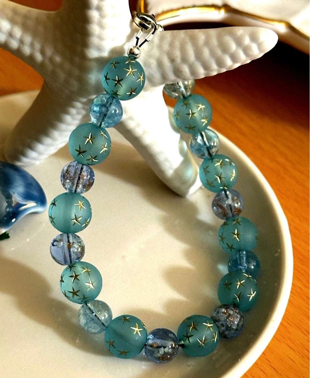 Blue and teal glass bead bracelet displayed upright on a starfish dish stand, highlighting bead color variation and handmade design