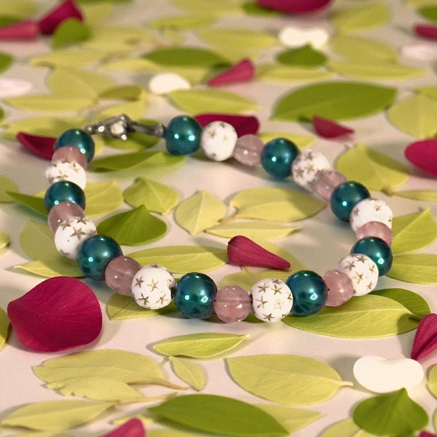 Teal and pink beaded celestial bracelet with white star-pattern beads photographed on a leafy natural background