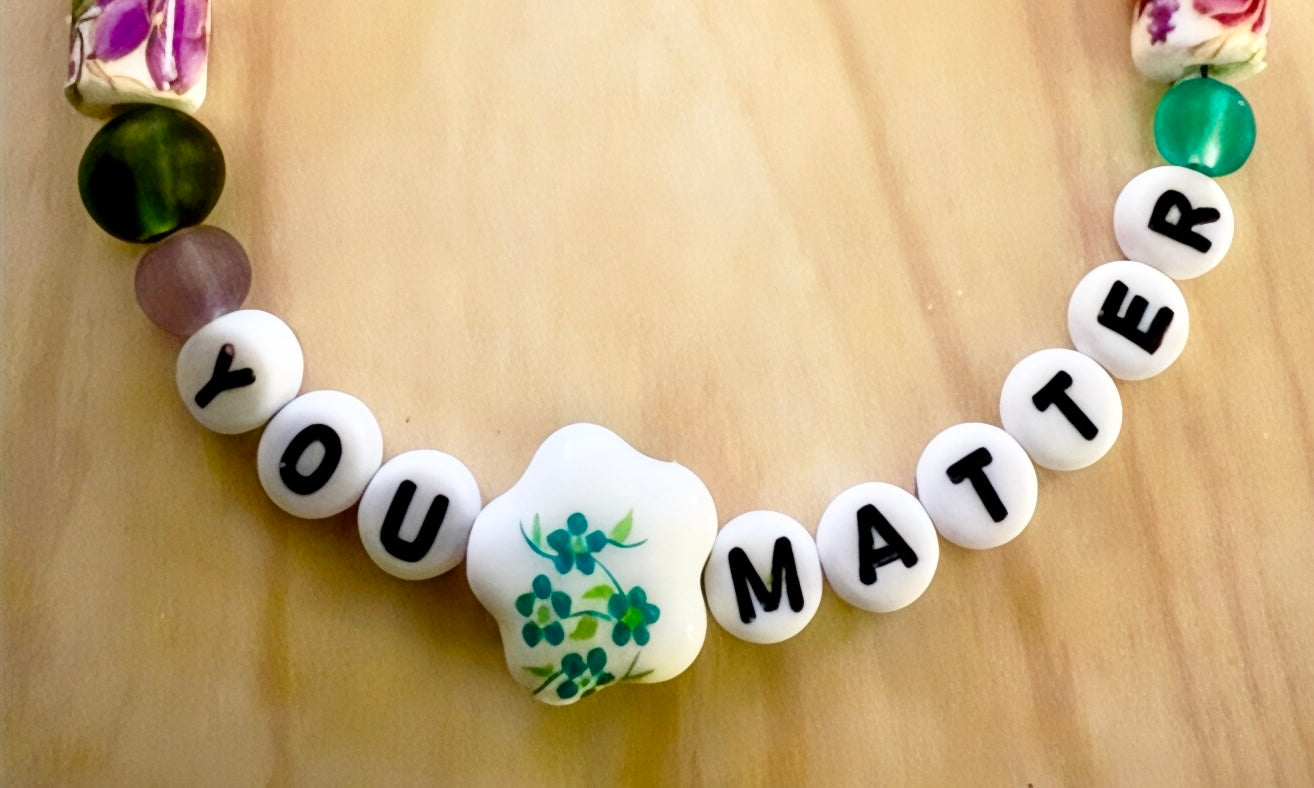 Close-up of a handmade “You Matter” beaded bracelet displayed in natural light, highlighting colorful beads and the affirmation message.