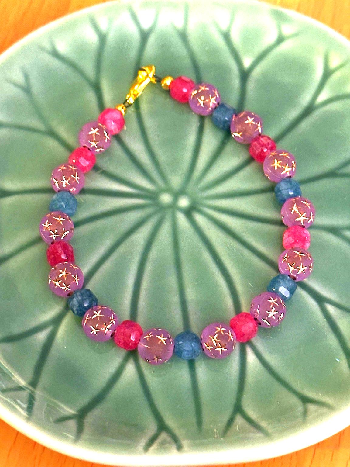 Handcrafted gemstone bracelet arranged on a green ceramic plate, highlighting pink, lavender, and teal tones.