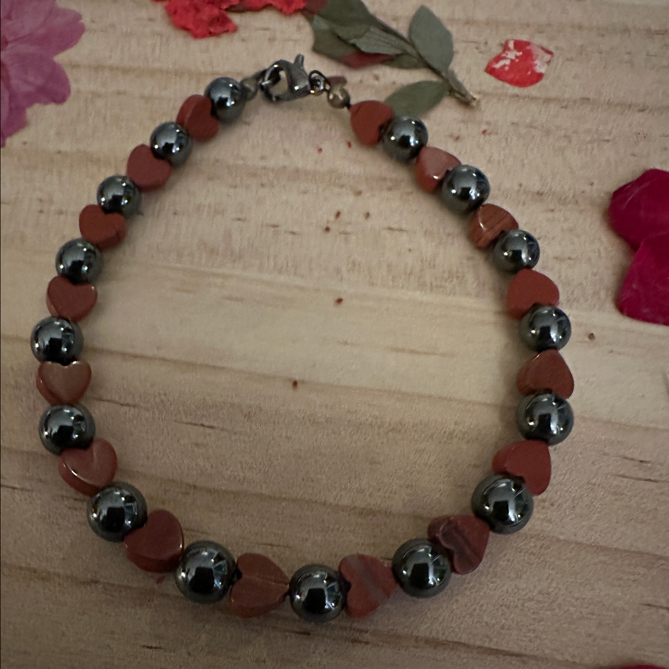 Handmade Quiet Heart bracelet with red heart beads and hematite stones arranged in a circle on a wooden surface