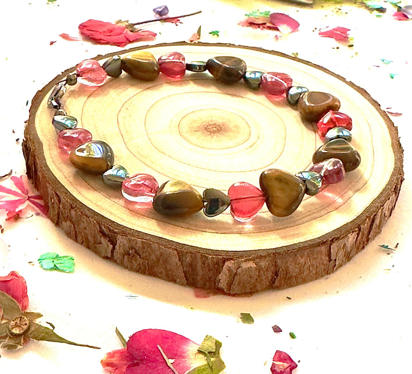 Romantic flat lay of Tiger Eye and pink heart bracelet with scattered petals and natural textures