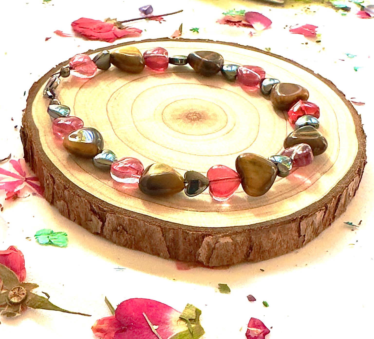 Romantic flat lay of Tiger Eye and pink heart bracelet with scattered petals and natural textures