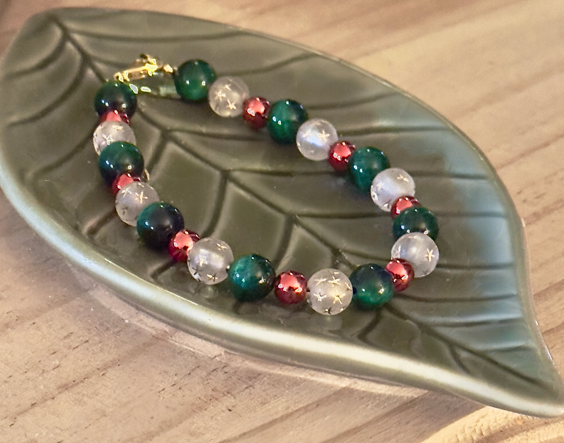 Close-up of handmade beaded bracelet on green ceramic leaf dish showing bead texture and polished finish.