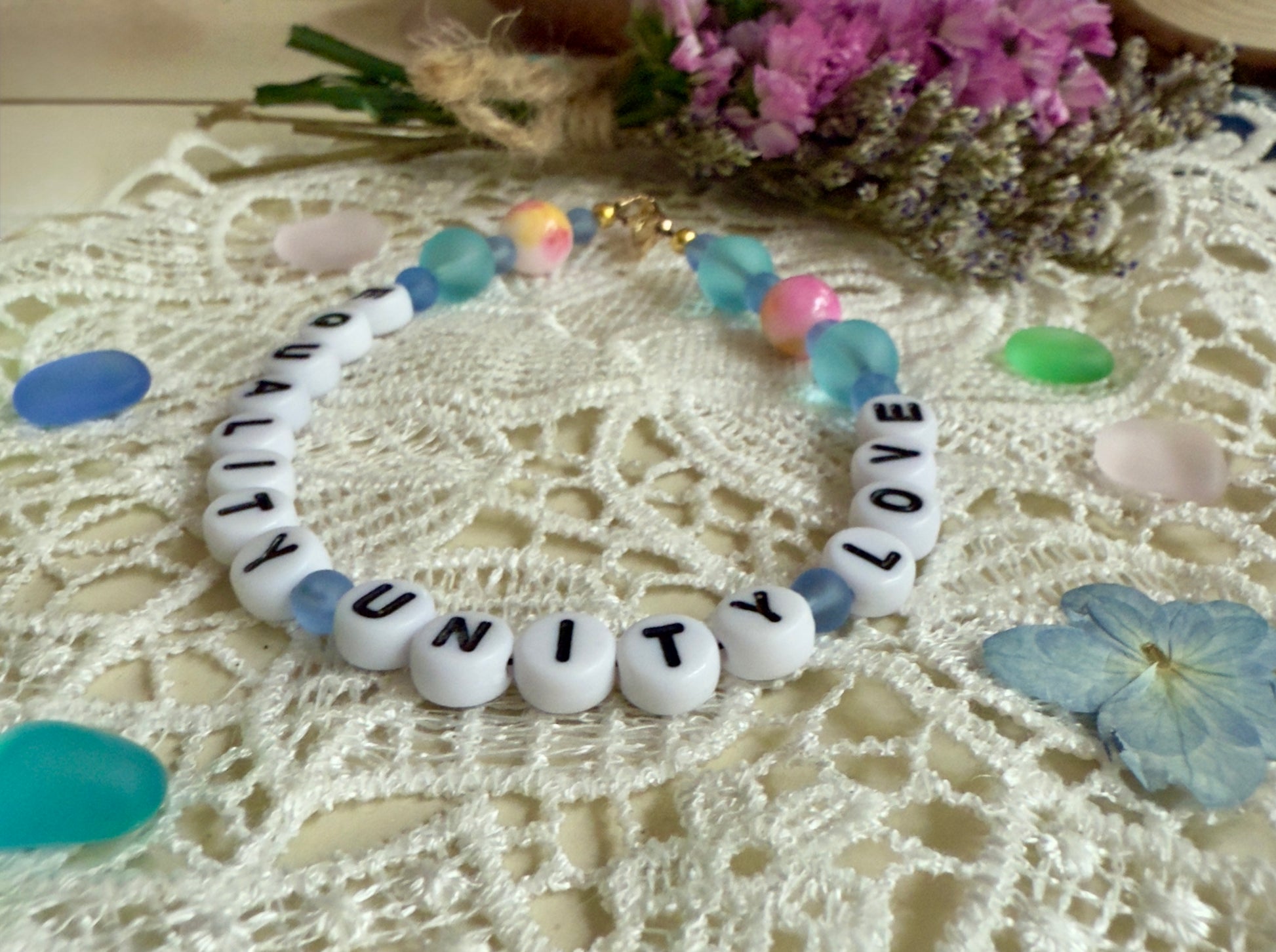 Equality Love Unity bracelet displayed in a soft lifestyle setting with dried flowers, emphasizing inclusivity and meaningful jewelry.