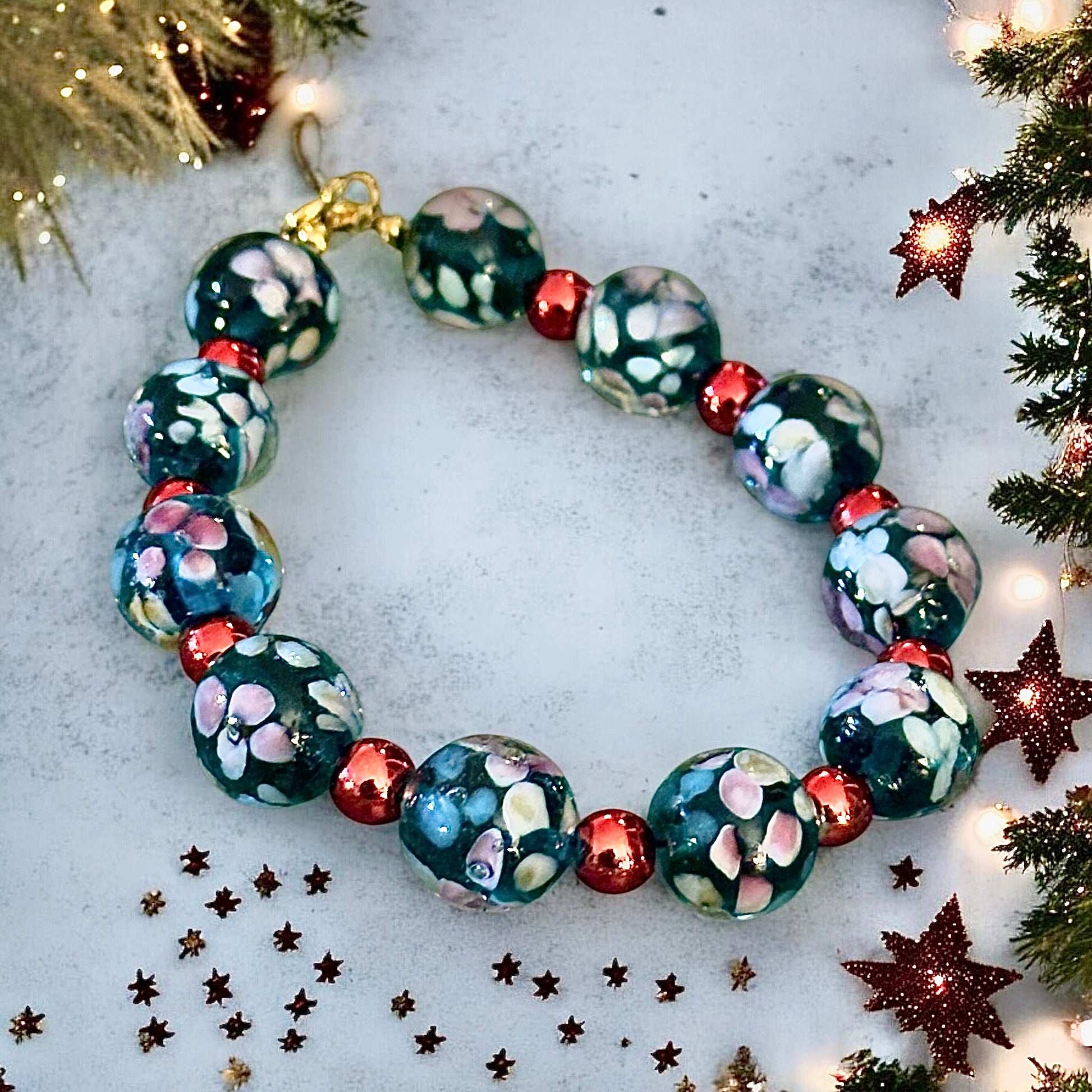 Winter-inspired flat lay of a handmade celestial bracelet surrounded by festive greenery and soft holiday decor.

