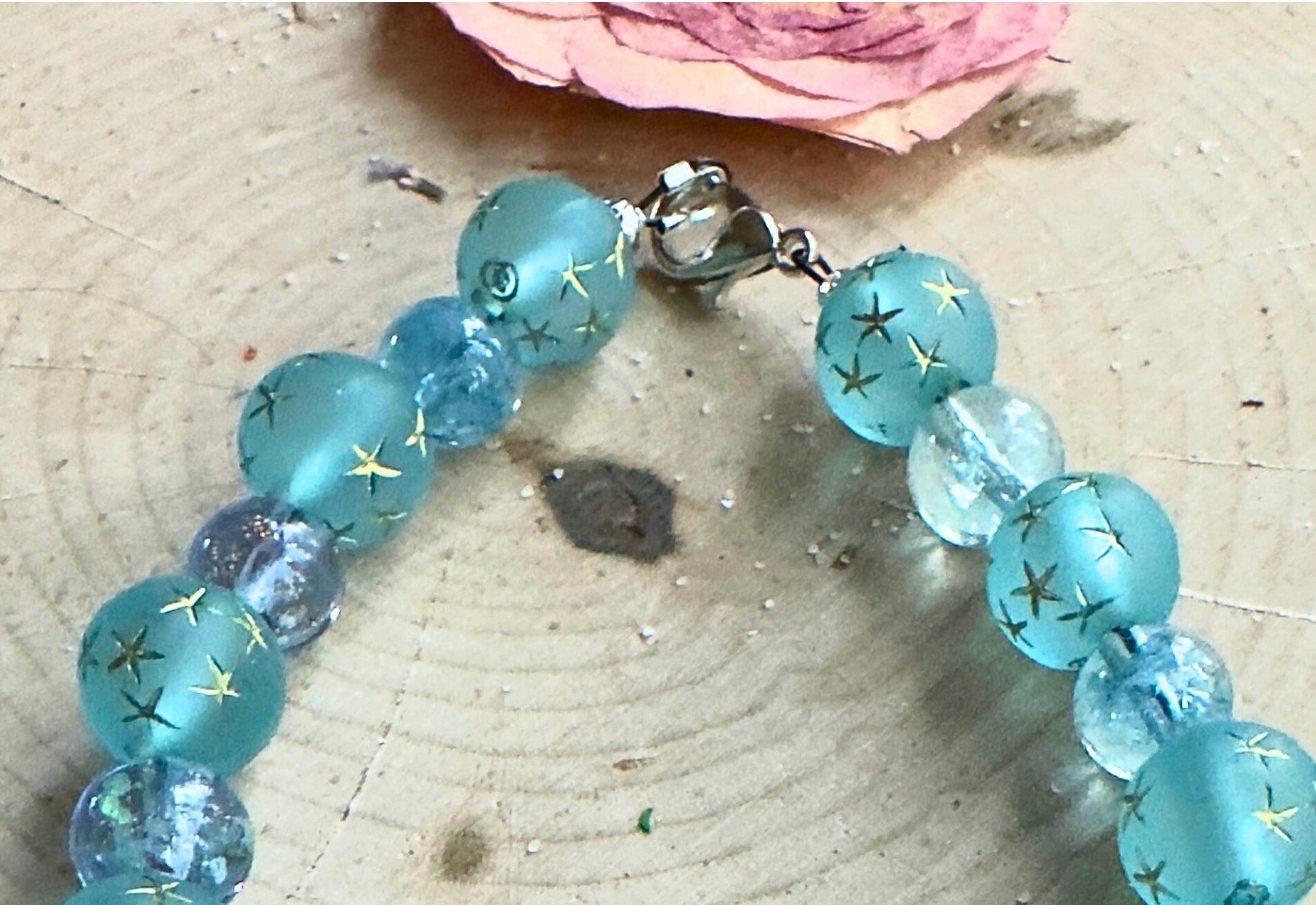 Close-up of handmade blue and teal glass bead bracelet showing clasp and bead details on a light wood surface