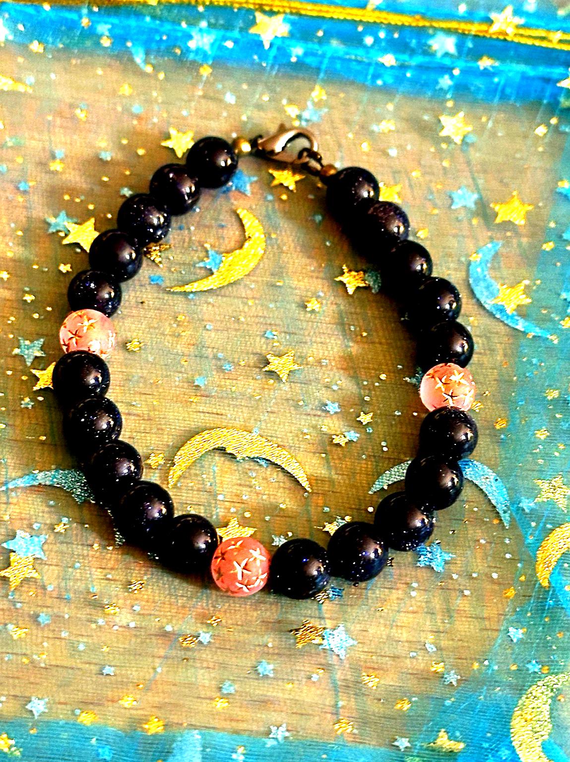 Celestial gemstone bracelet on a moon-and-stars background, featuring deep blue sandstone beads and pink accent beads