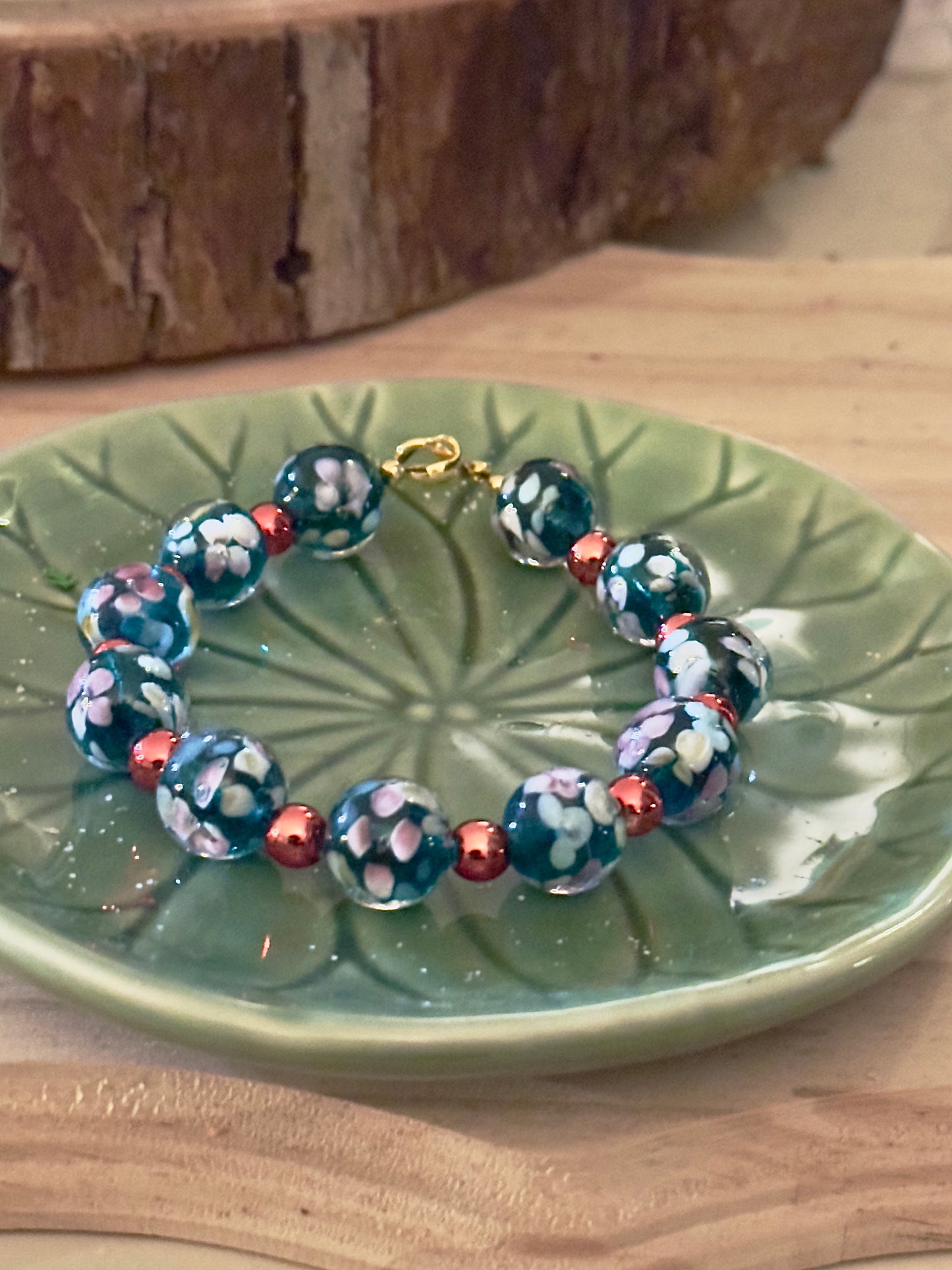 Handcrafted floral glass bead bracelet photographed on a green ceramic plate in natural indoor lighting.