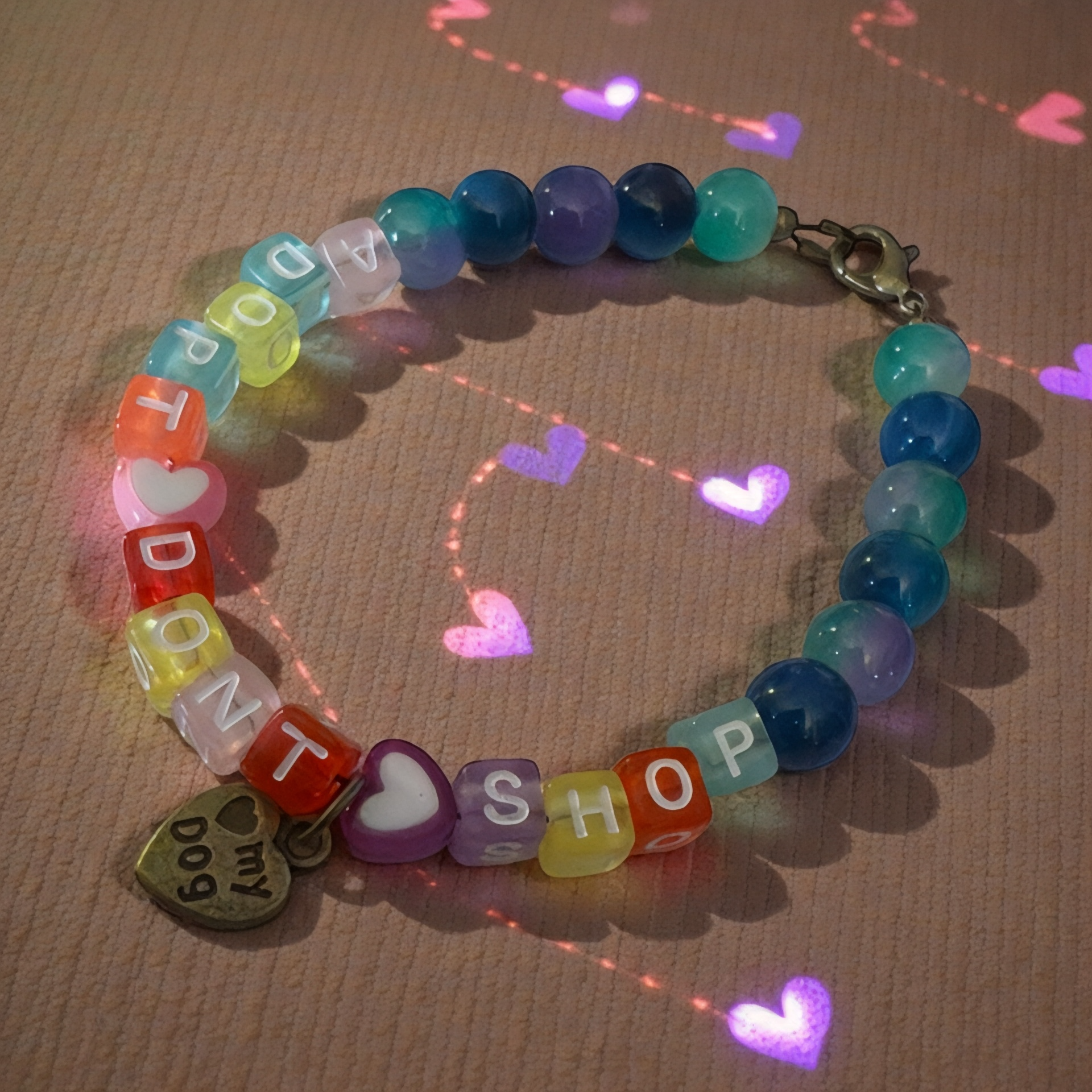 Close-up of colorful letter beads spelling “Adopt Don’t Shop” on a handmade bracelet with heart bead and paw charm.
