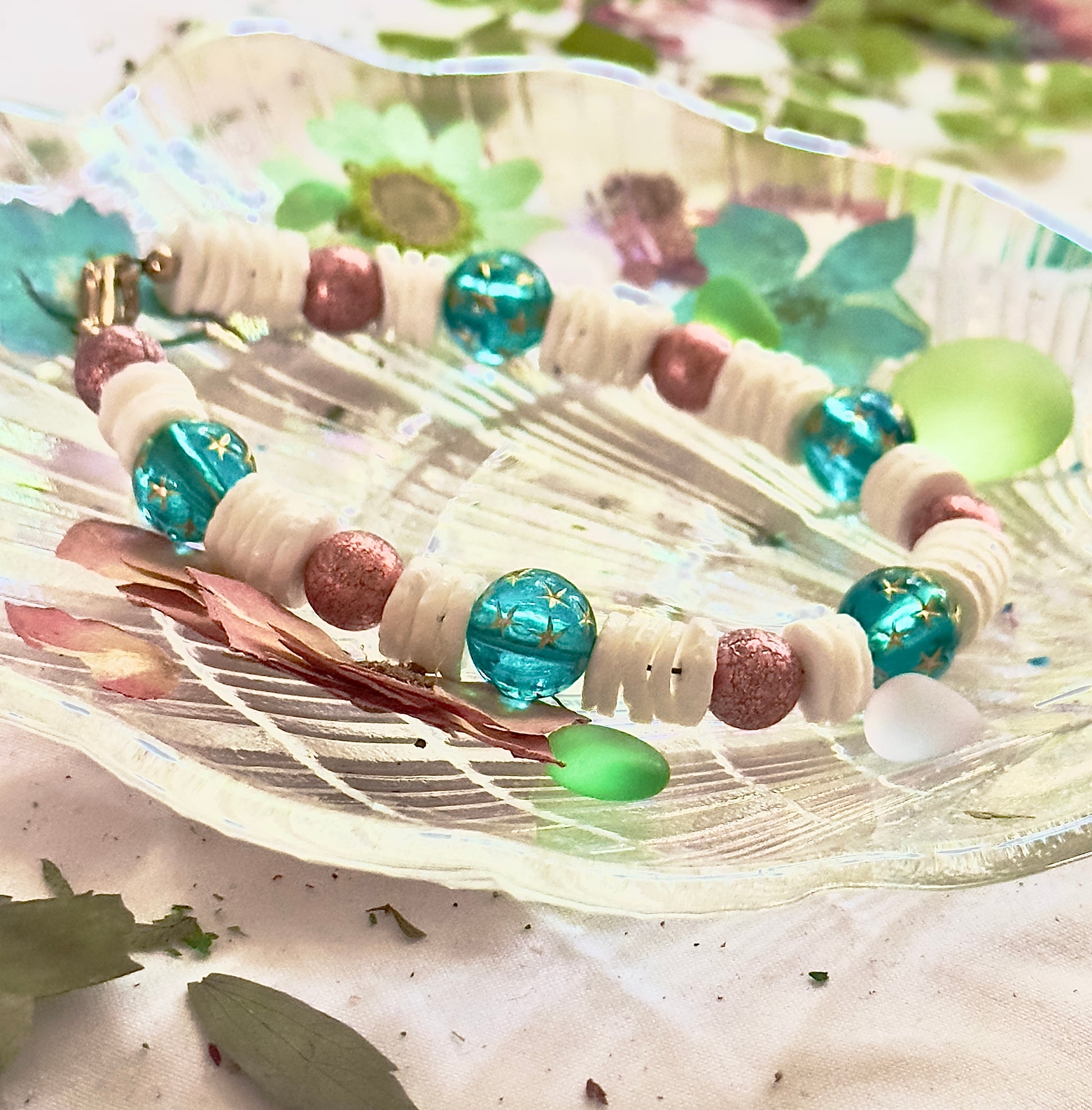 Handmade ocean-themed bracelet with teal star beads and white shell spacers styled outdoors with greenery and natural light.
