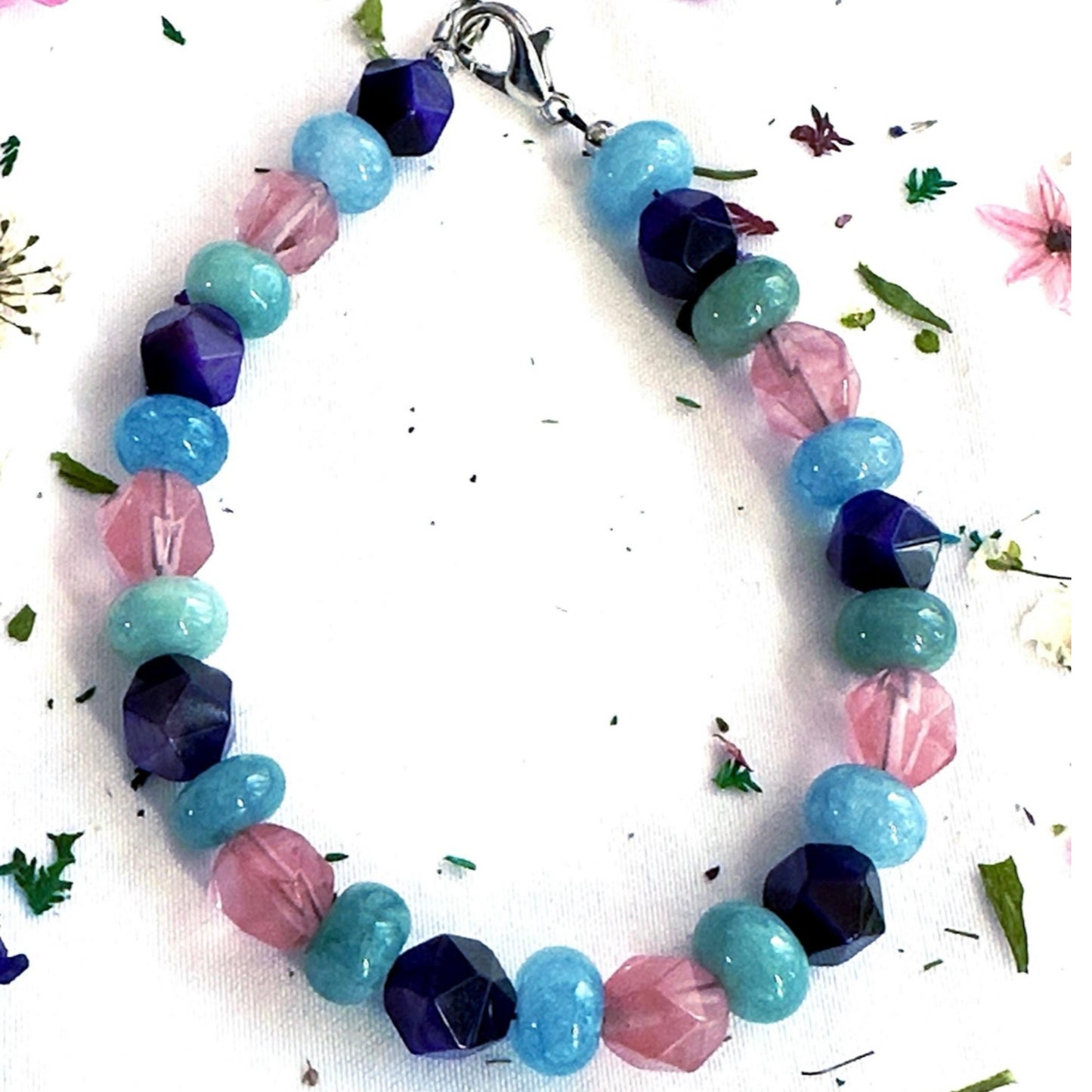 Handmade gemstone bracelet with pink, teal, and deep blue beads on a light neutral background, minimalist product photo