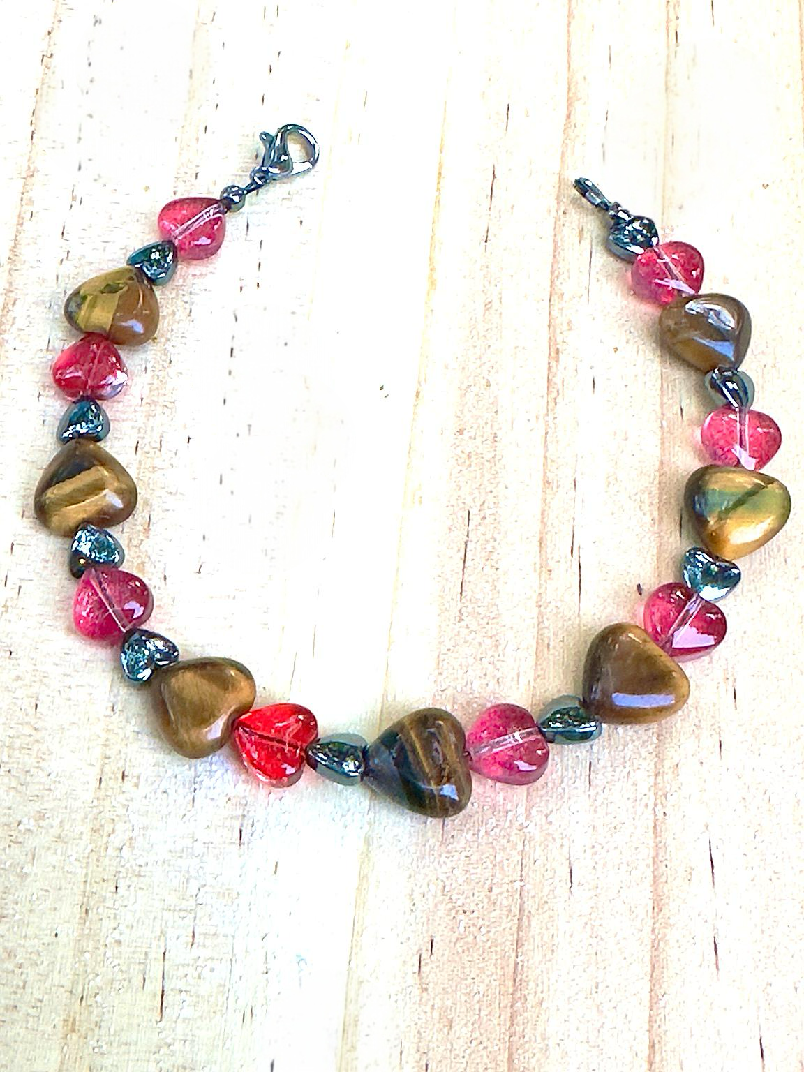 Handmade Tiger Eye and pink heart bracelet laid flat on a light neutral background, Rooted in Harmony Anchored in Love