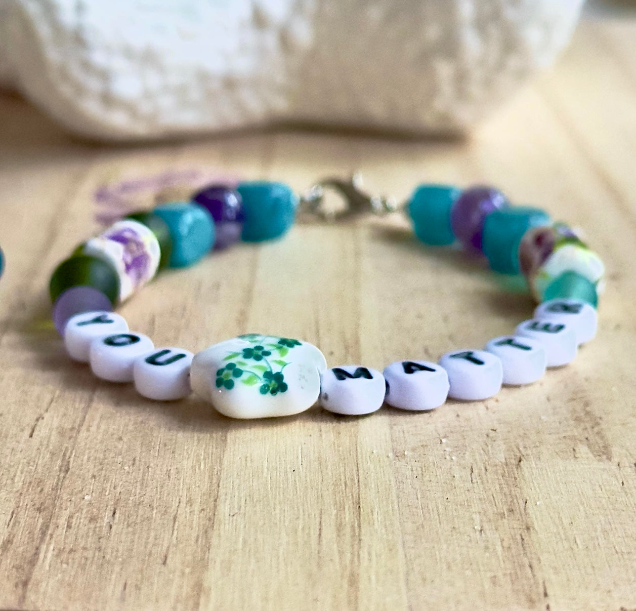 Lifestyle photo of a handmade “You Matter” bracelet worn on the wrist while two people hold hands outdoors, symbolizing connection, comfort, and support.