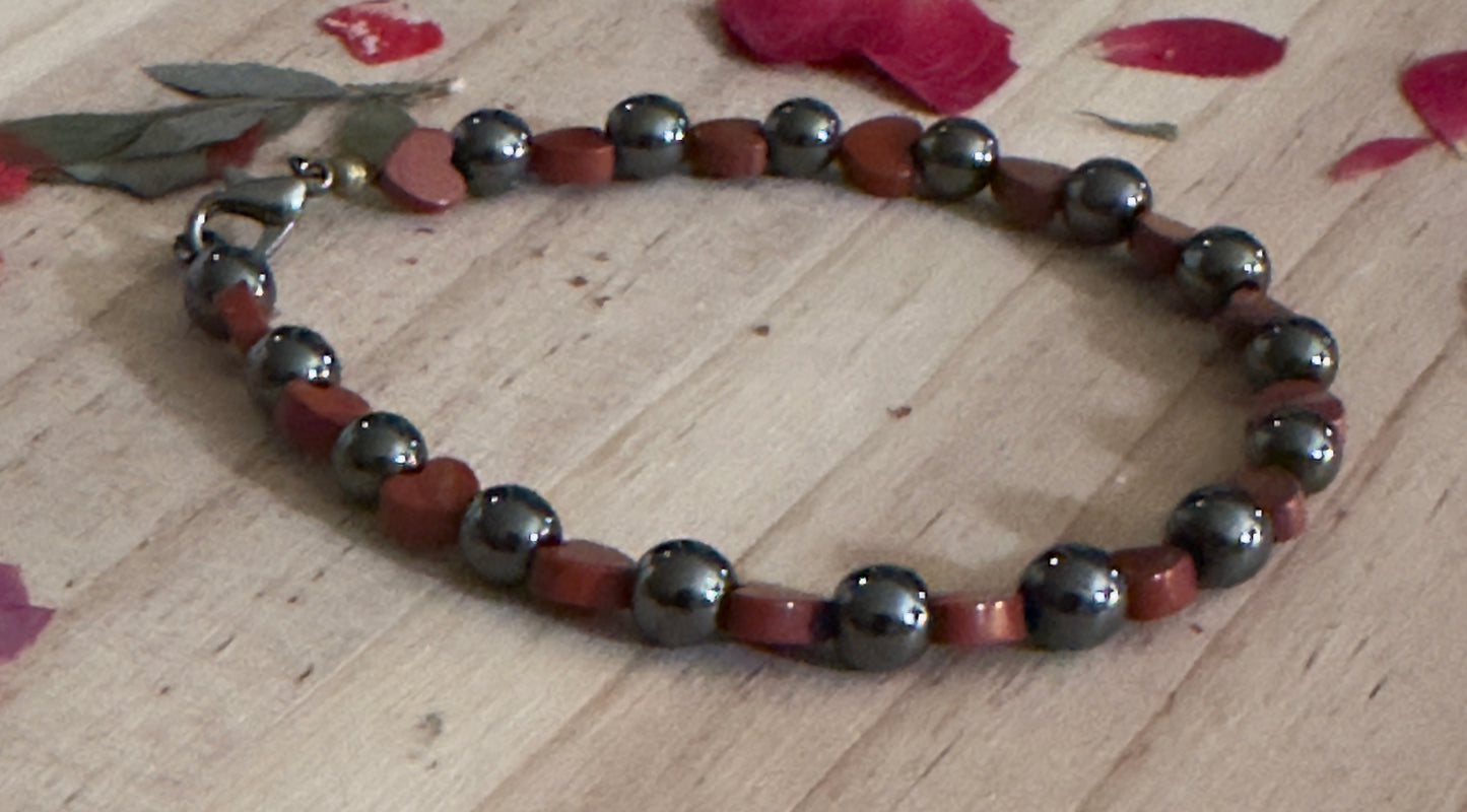 Bracelet with red and black beads on a wooden surface with pink petals.
