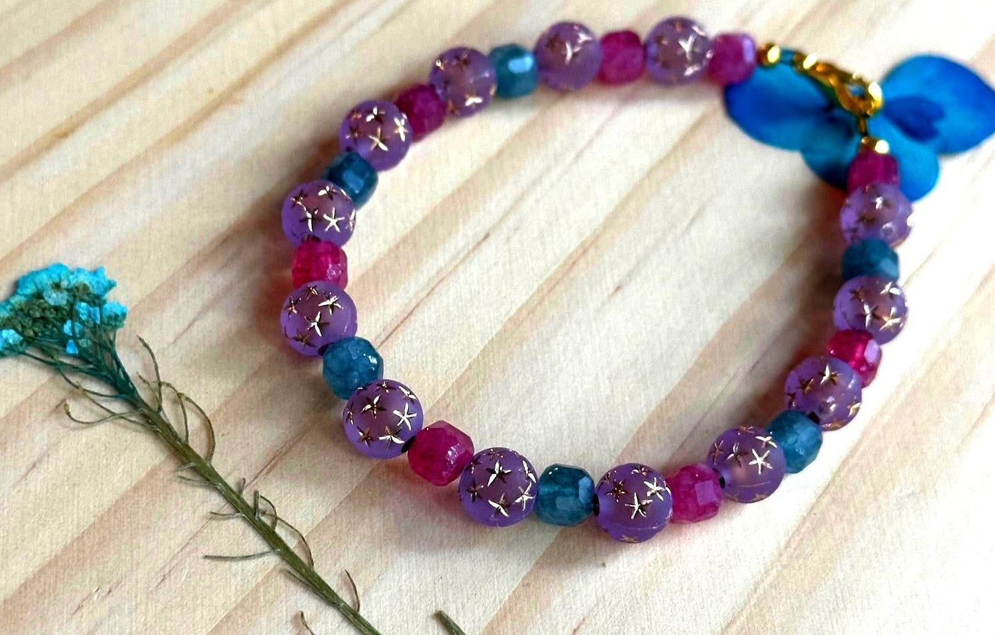 Aurora Goddess bracelet styled with dried blue flower on soft wood background