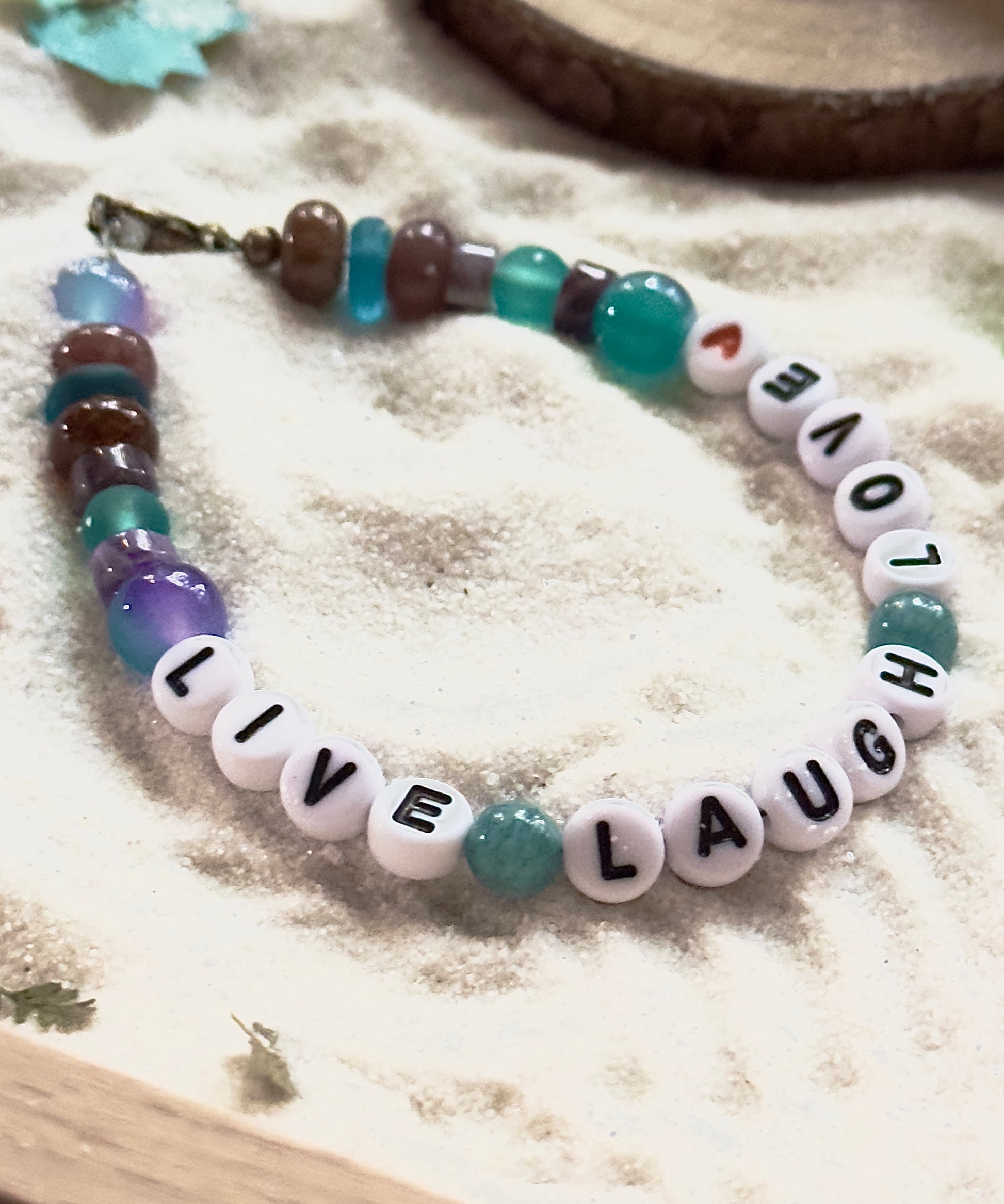 Live Laugh Love gemstone bracelet styled on soft natural fabric with coastal-inspired textures.