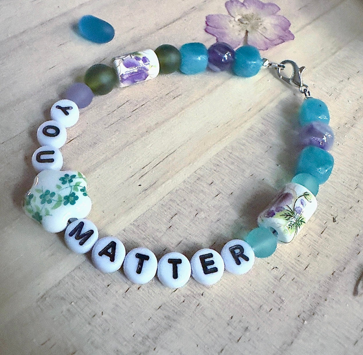 Lifestyle photo of a handmade “You Matter” bracelet worn on the wrist while two people hold hands outdoors, symbolizing connection, comfort, and support.