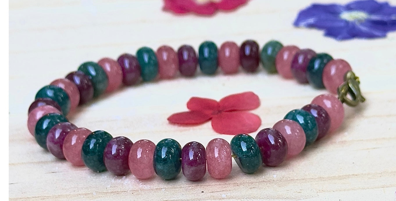 Ocean-inspired Between The Waves bracelet arranged in a circle around a pink flower, highlighting colorful gemstone rondelle beads.