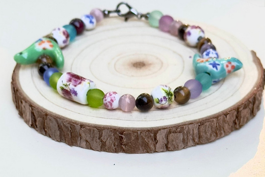 Bird-Eye View colorful beaded bracelet with turquoise bird and floral beads displayed on a natural wood slice.