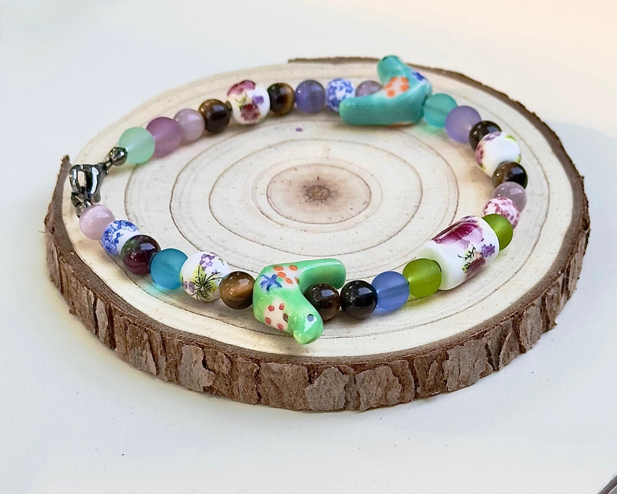 Bird-Eye View handmade bracelet featuring colorful beads, floral accents and turquoise ceramic birds on a wood slice.