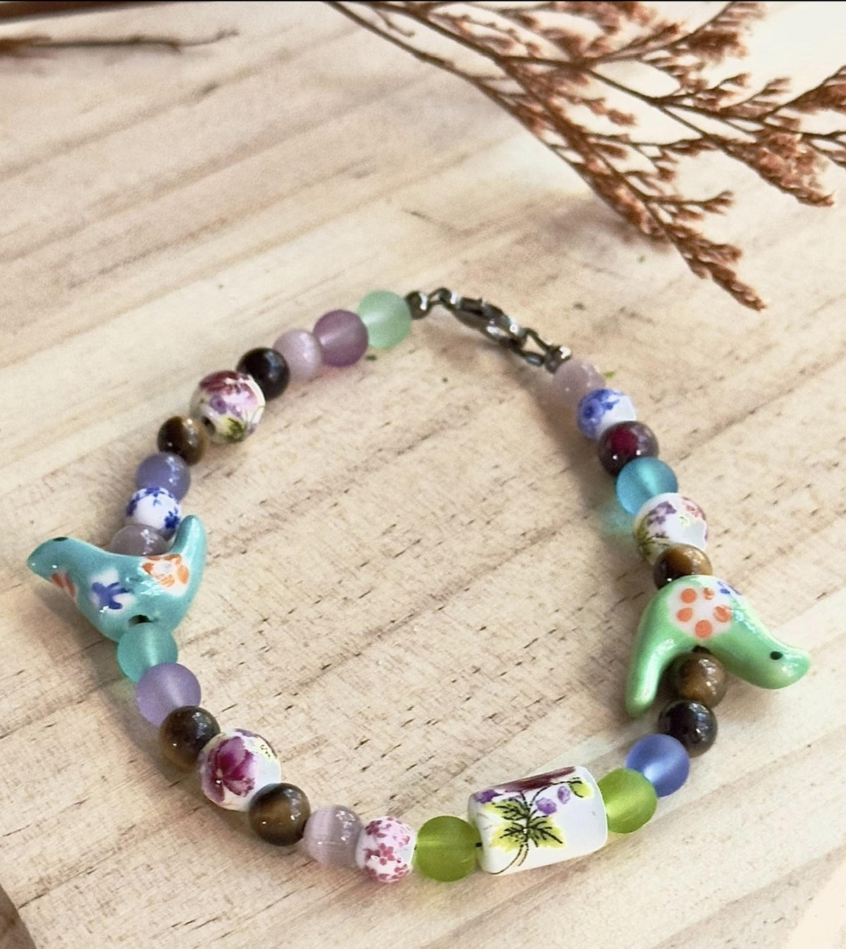 Colorful Bird-Eye View bracelet laid flat on a natural wood surface to show the full bead and bird design.