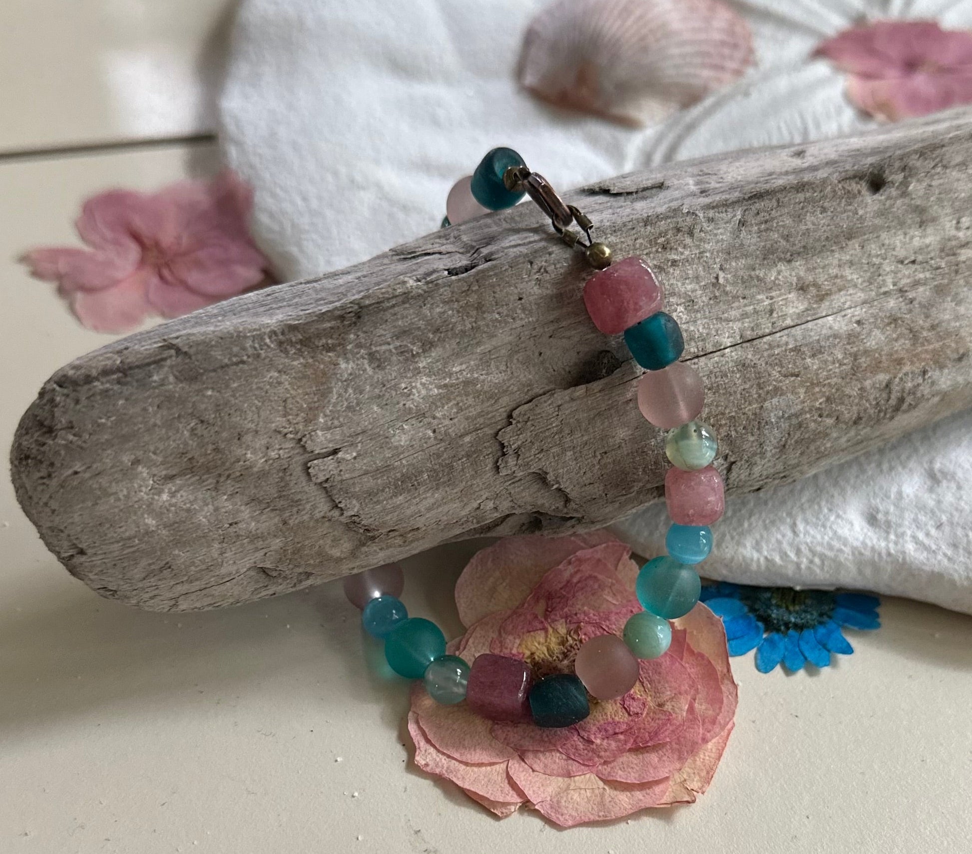 Beaded bracelet with pink and blue beads on a piece of driftwood with pink petals.