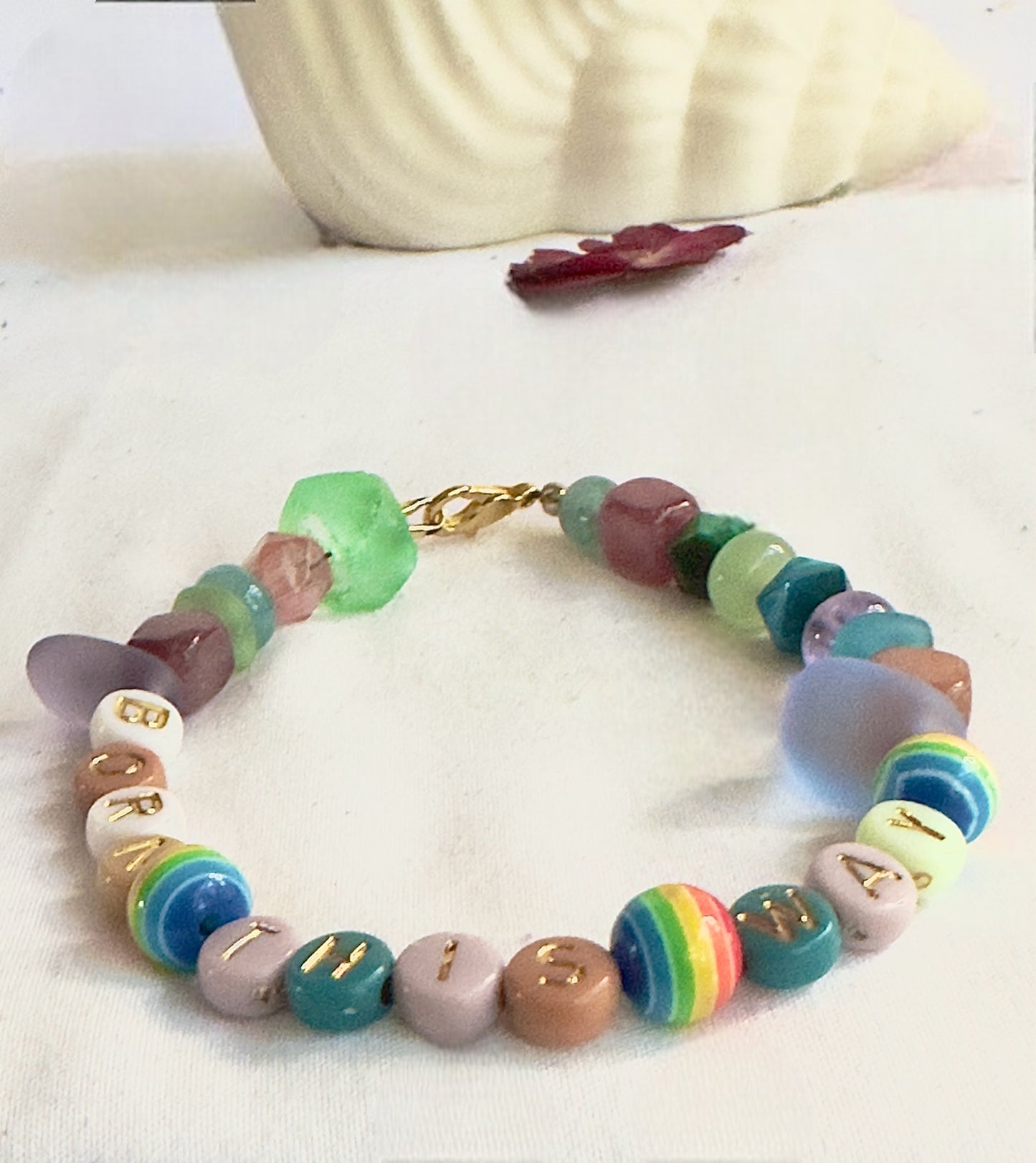 Born This Way Pride bracelet displayed on soft white fabric  with shell coastal-inspired styling.