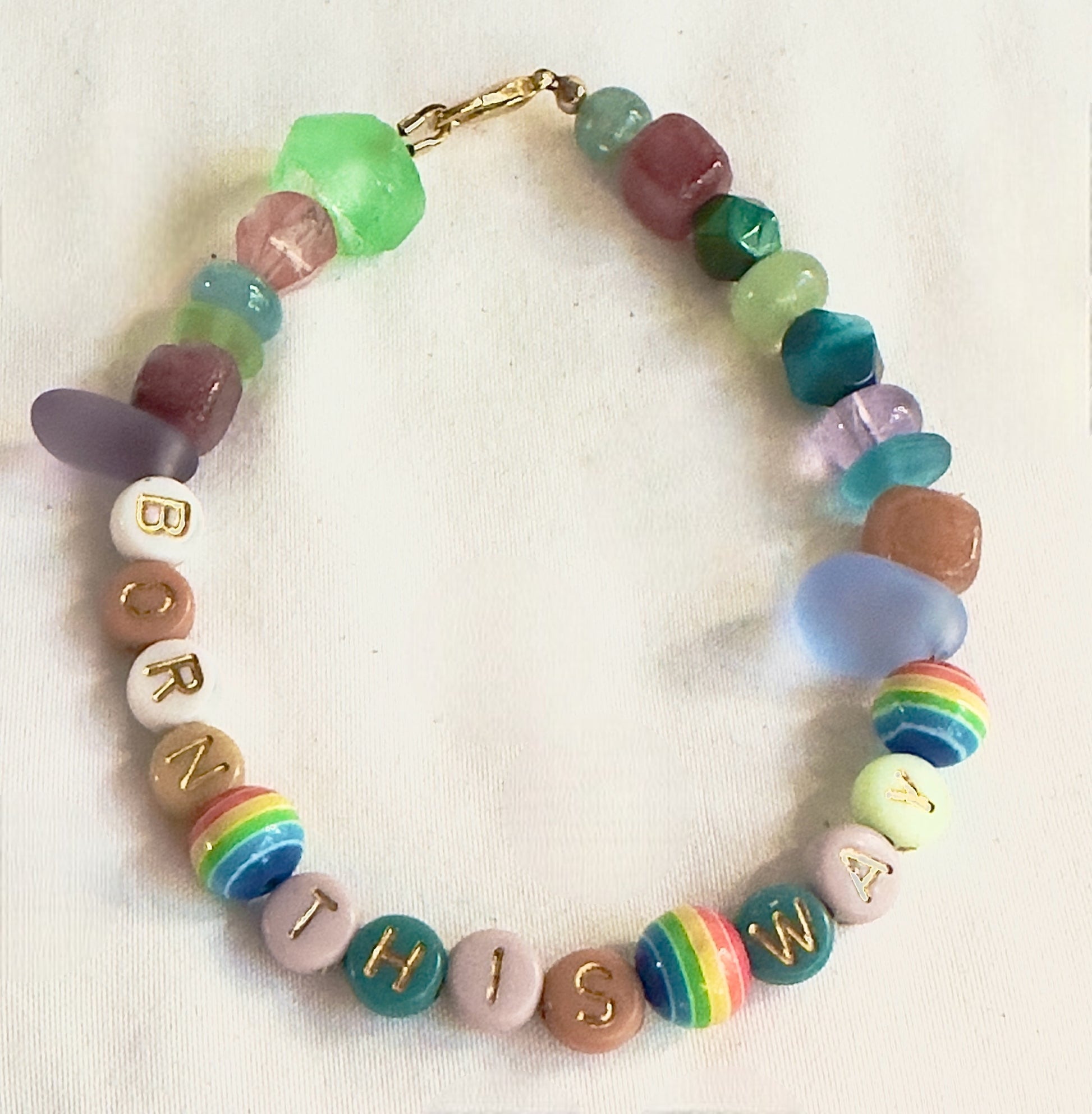 Handmade Born This Way Pride bracelet featuring rainbow accent beads, pastel letter beads, and colorful gemstone-inspired beads arranged in a circle.
