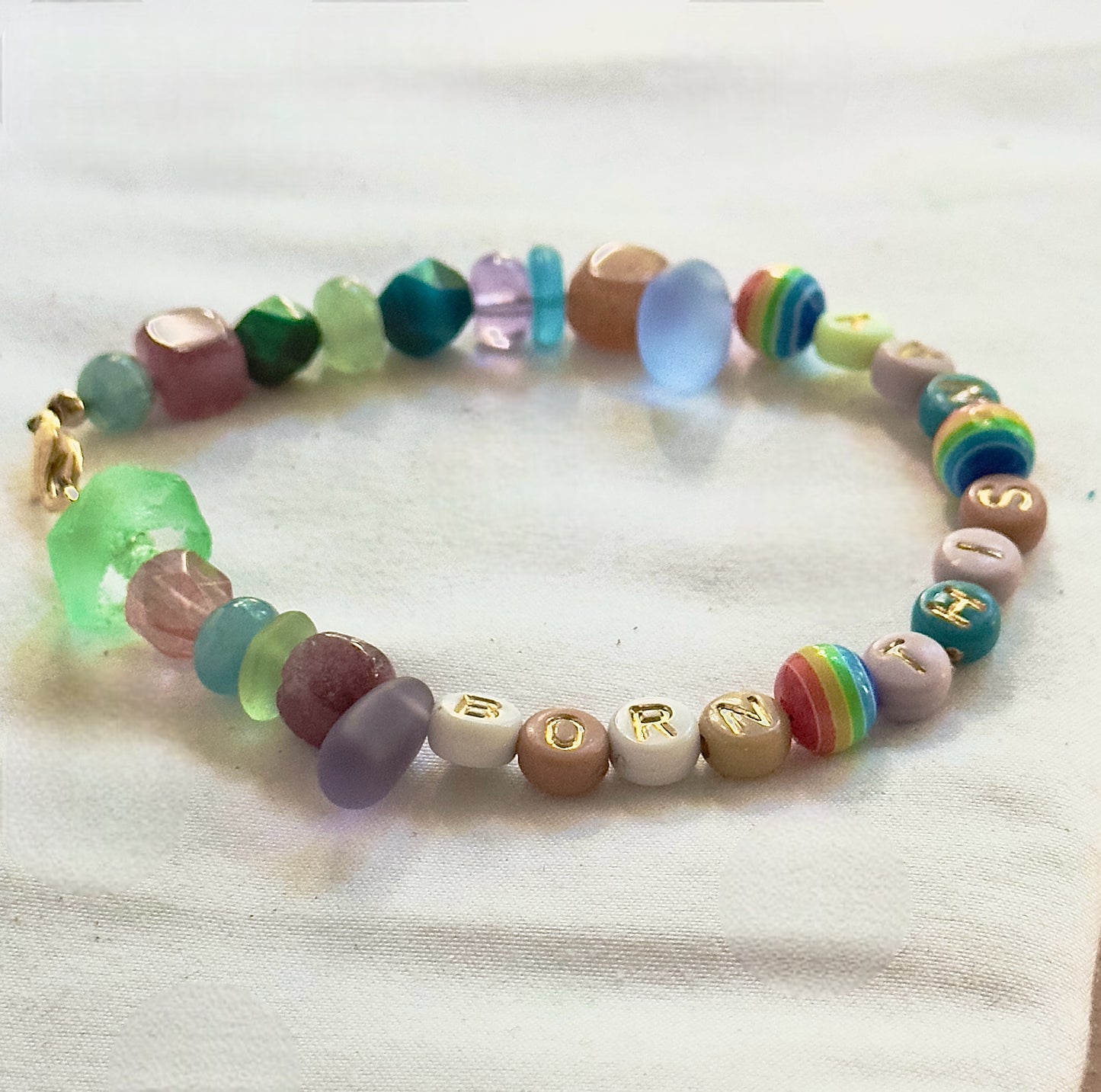 Side view of handmade Pride bracelet showing rainbow beads, colorful glass beads, and Born This Way lettering.