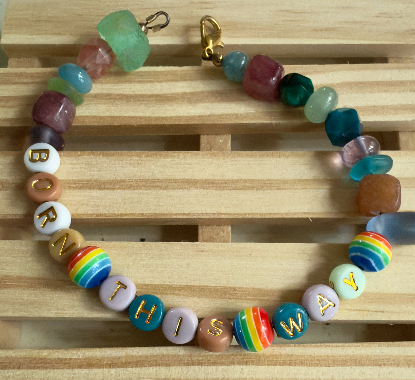 Colorful beaded bracelet with letter beads spelling 'BORN THIS WAY' on a wooden surface