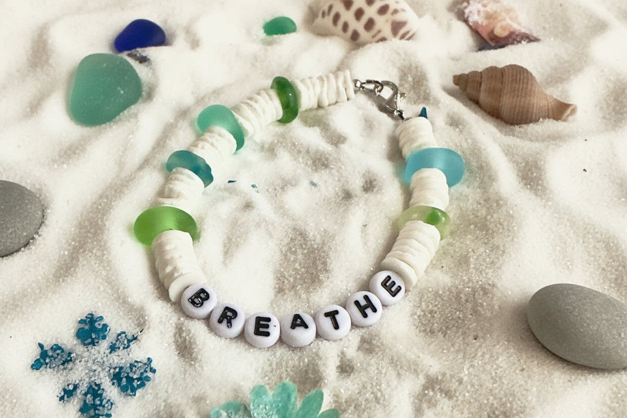 Ocean inspired Breathe bracelet with white beads, aqua and green accents styled in sand with coastal elements