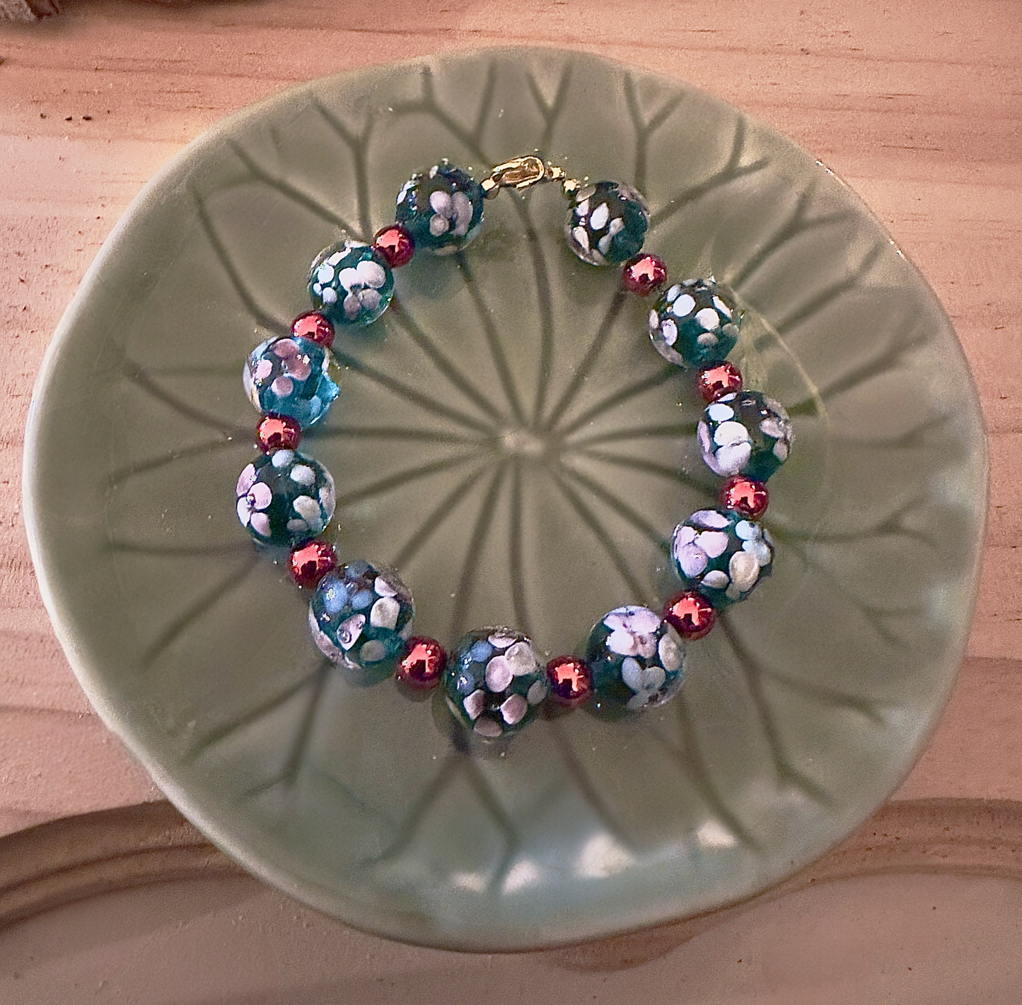 Handmade winter celestial bracelet displayed on a green ceramic plate, featuring blue floral glass beads and copper accent beads.