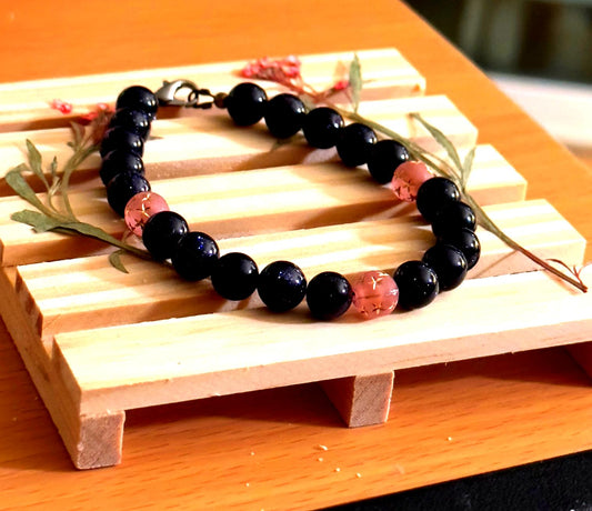Handmade dark blue sandstone bracelet with pink star-etched beads displayed on a small wood decor