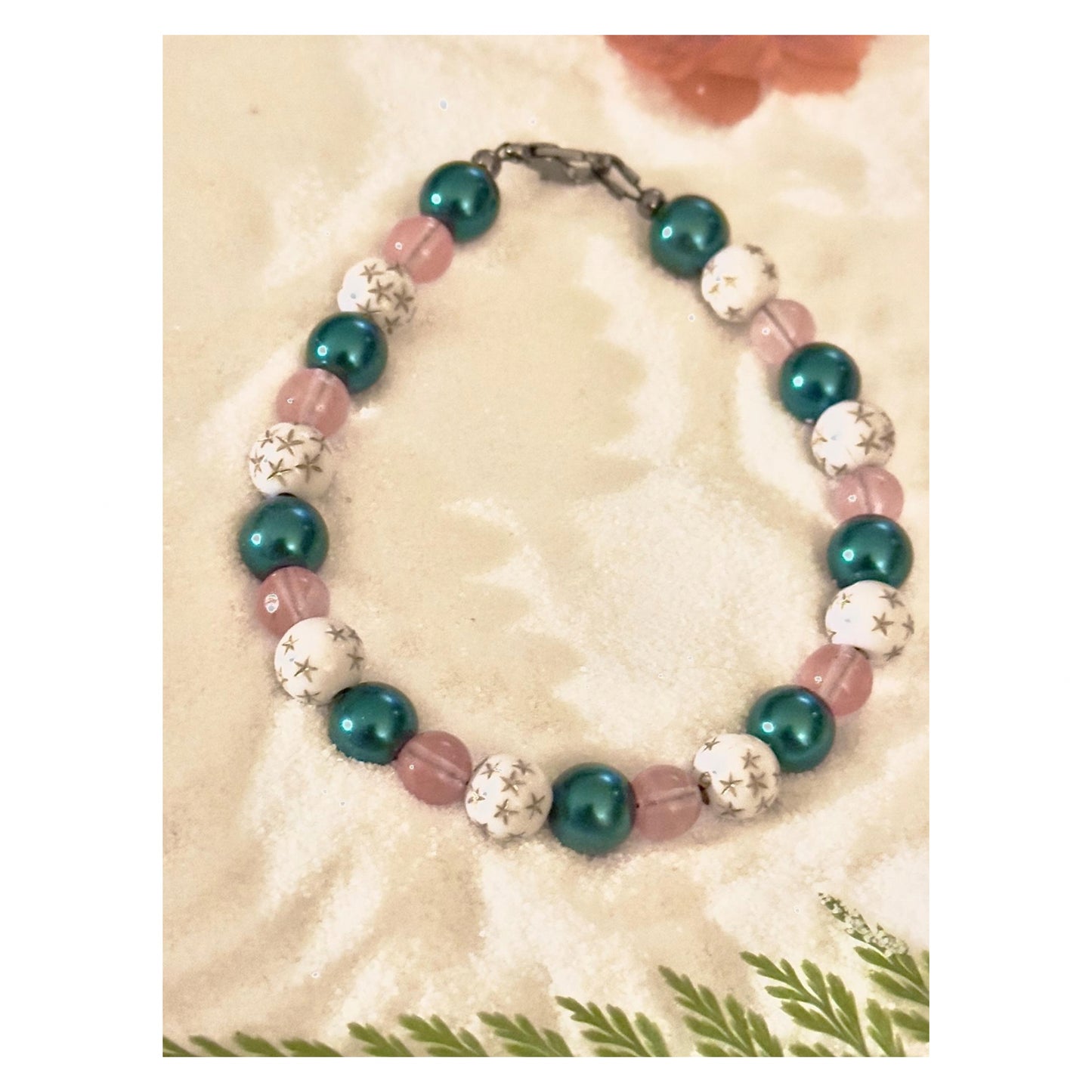 Handmade celestial bracelet with teal pearl beads, soft pink accents, and white star-pattern beads displayed on a neutral background